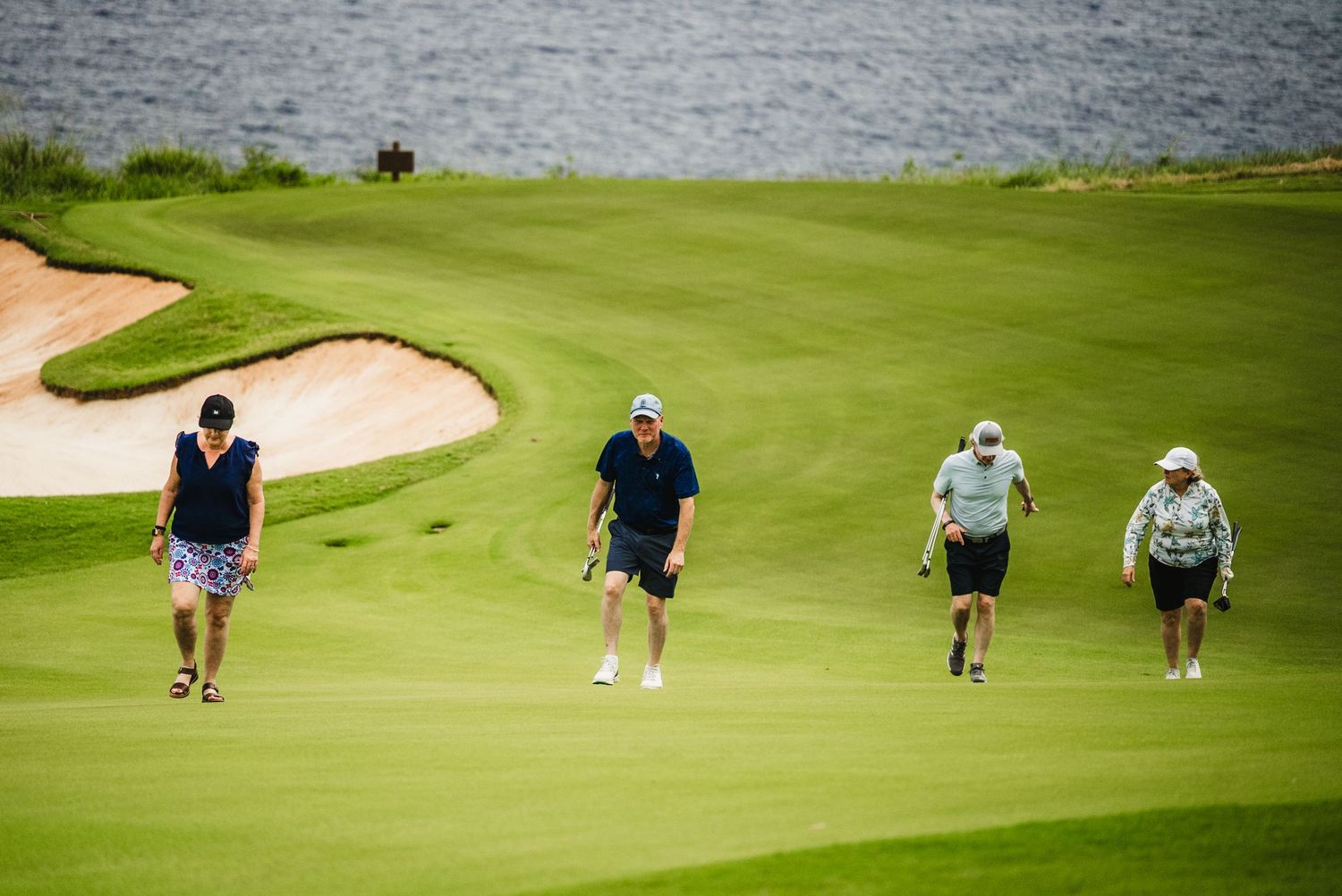 A set of 4 golfers walking up a hill with the ocean in the background at the golf course on Lanai in Hawaii.