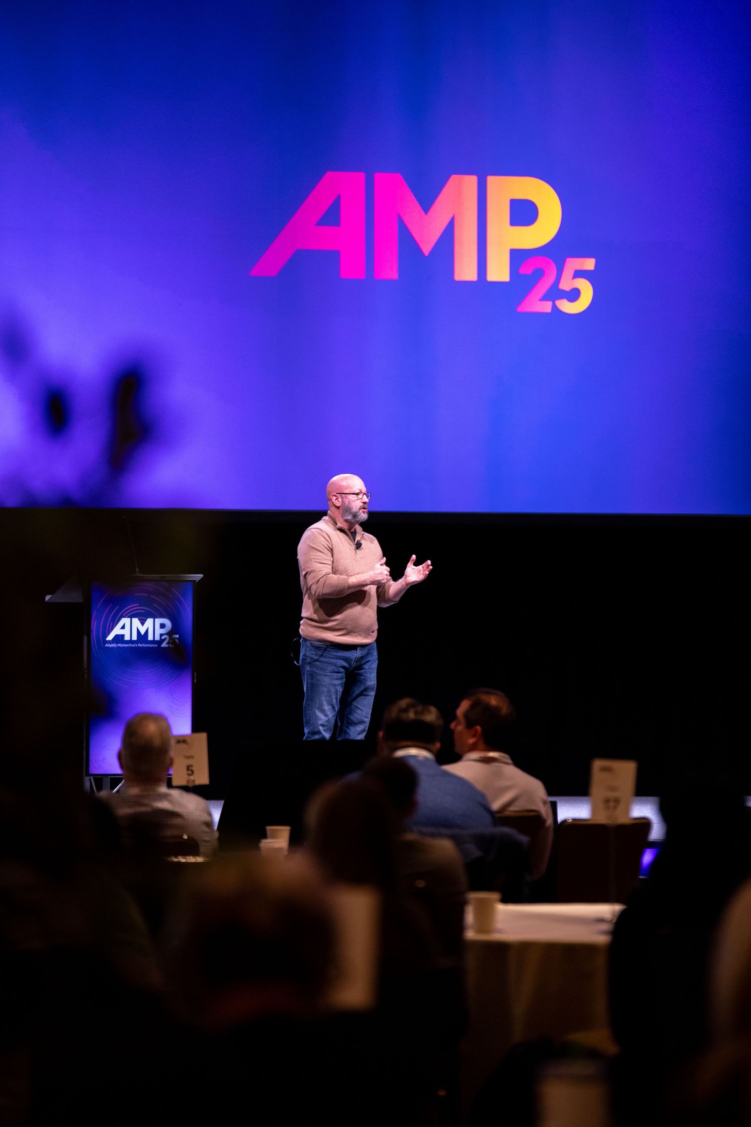 Man talking on stage with event branding on screen behind him