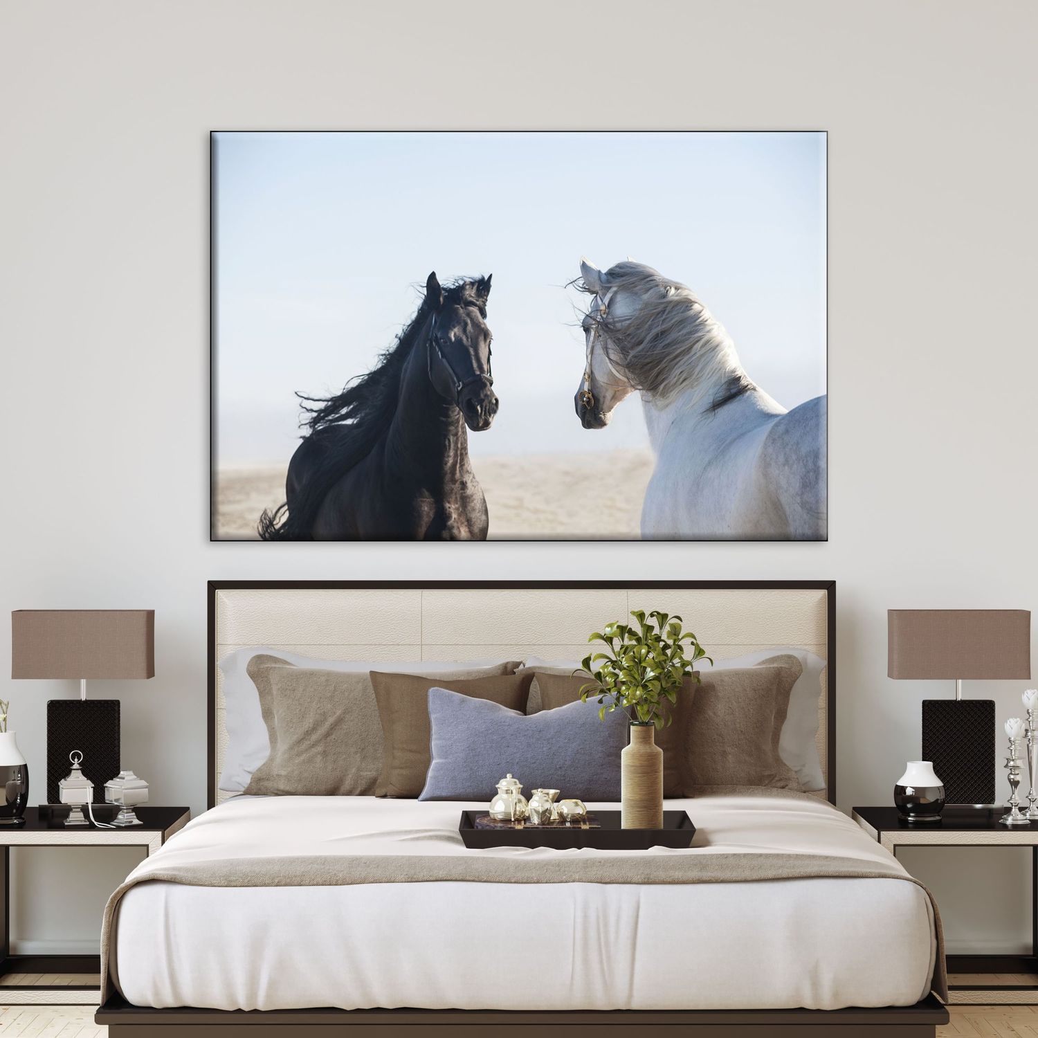 Black and white horses facing each other in desert landscape canvas wall art above a neutral toned bedroom bed.