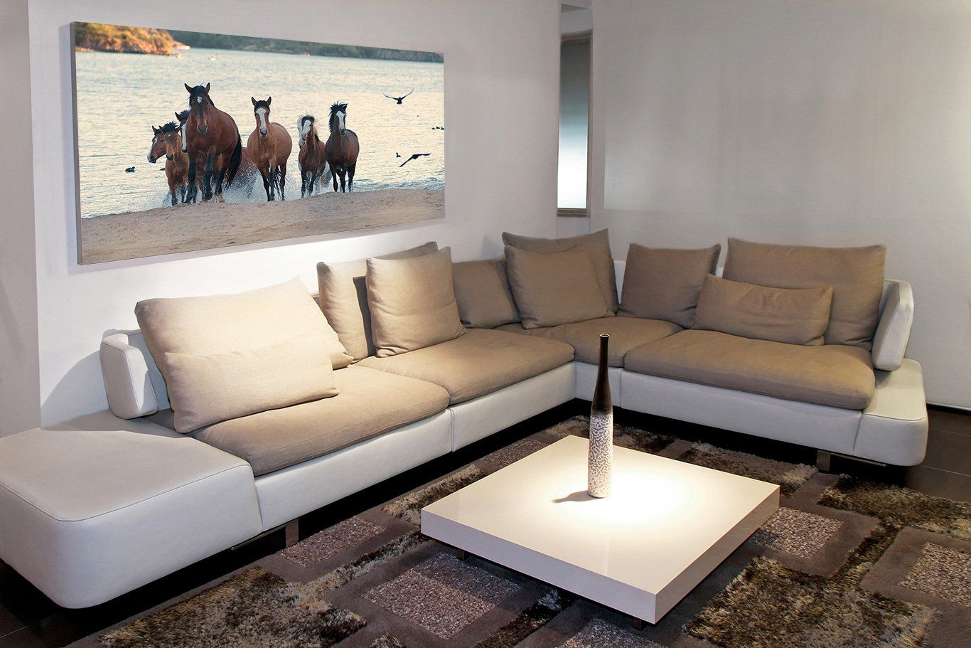Modern living room with beige sectional sofa, white coffee table, and a large canvas print of wild horses on the wall.