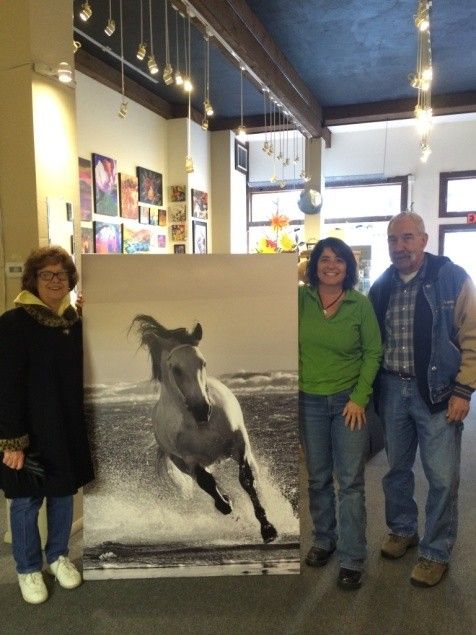 Three people posing beside a large black and white horse photograph print inside an art gallery.
