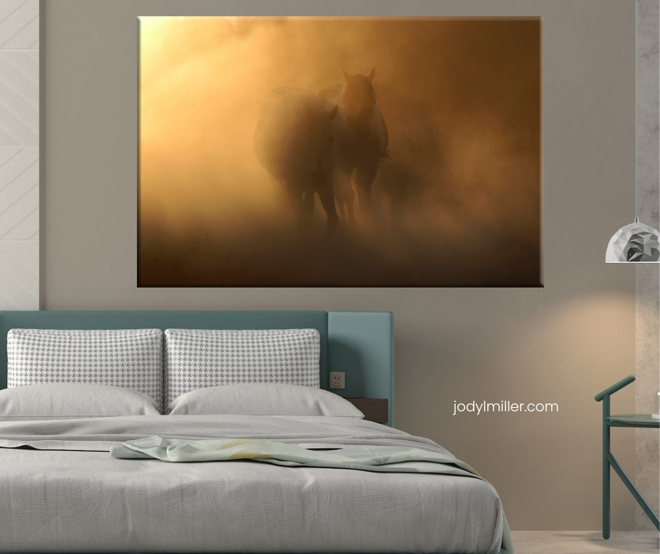 Dramatic canvas wall art of horses in golden misty fog above a bed, from jodylmiller.com, in a modern bedroom.