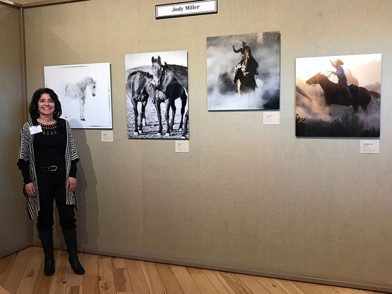Photographer, Jody Miller standing beside horse photography prints displayed at an art exhibition at The Phippen Museum in Prescott, AZ
