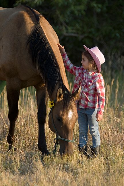 Young girl petting her horse while it grazes