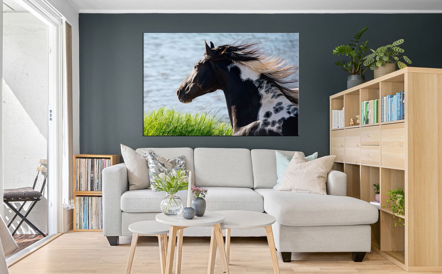 A black and white spotted horse with flowing mane runs near water, displayed as large canvas wall art in a modern living room.