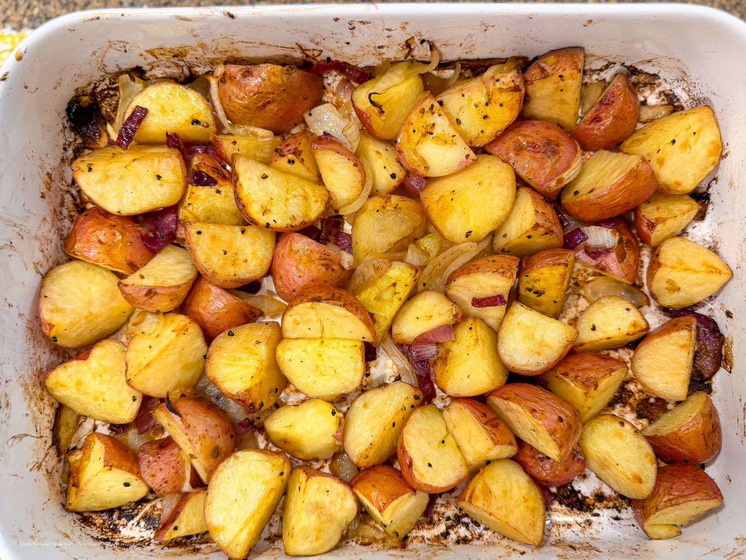 Roasted red potatoes with herbs and onions baked golden brown in a white rectangular baking dish.
