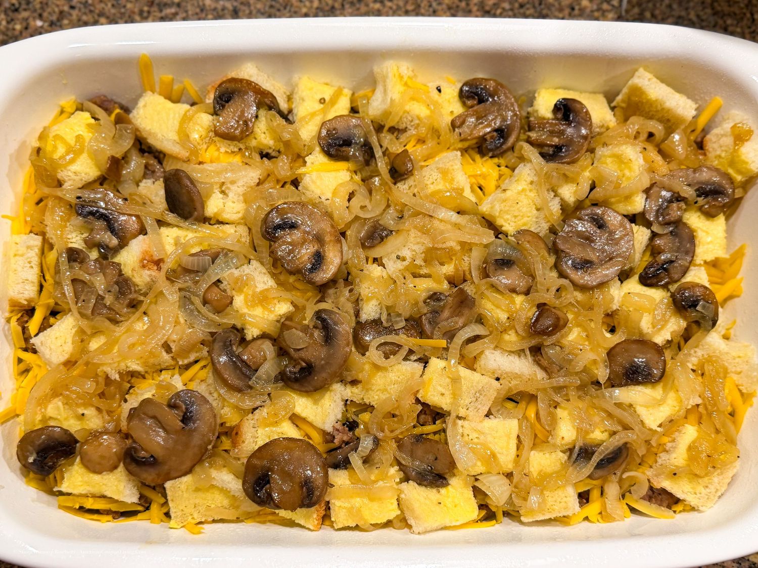 Baked casserole dish with egg, sliced mushrooms, caramelized onions, and cheese in a white rectangular pan.