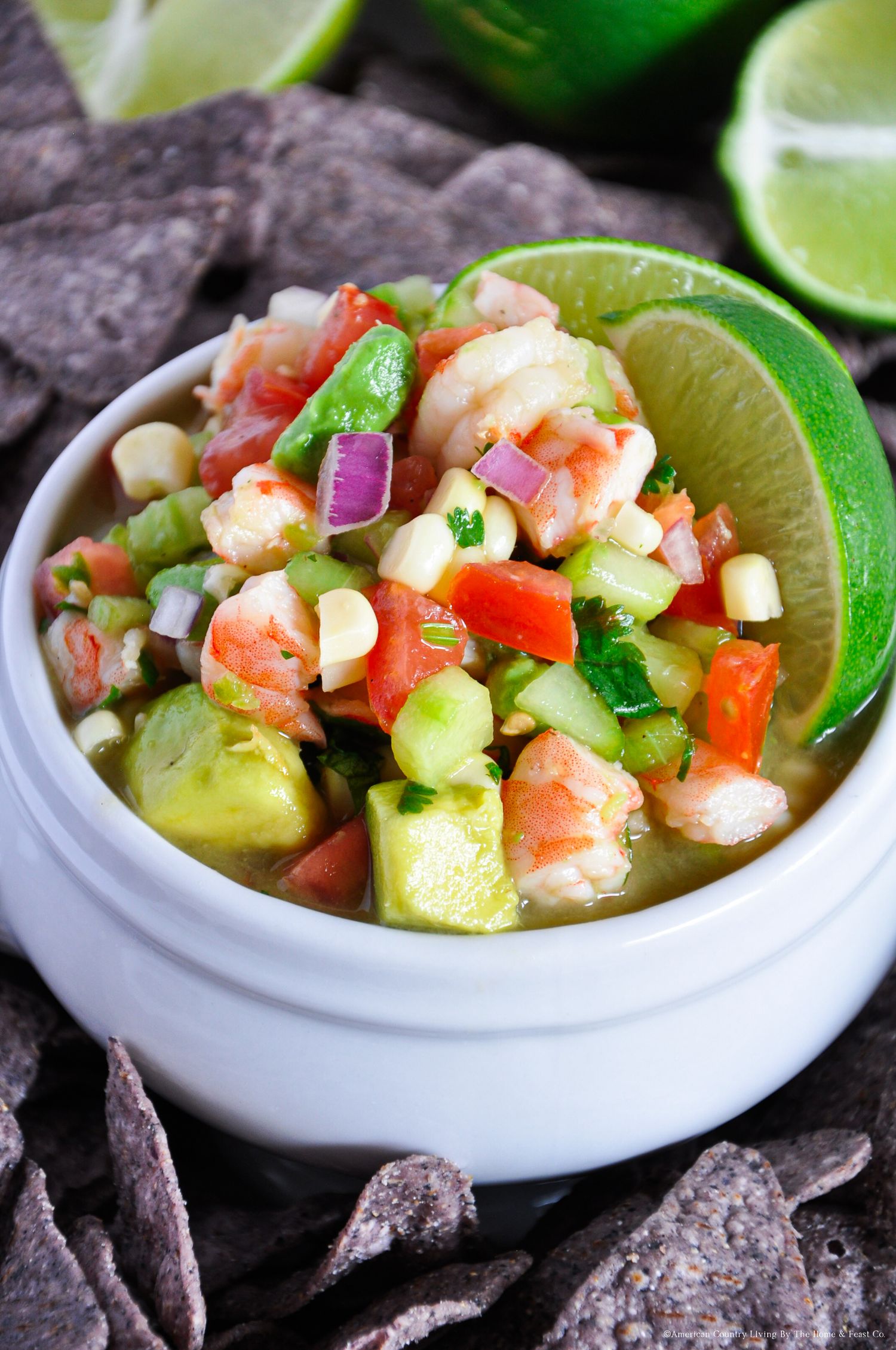 Vibrant shrimp ceviche with diced vegetables and lime wedges served with blue corn chips.
