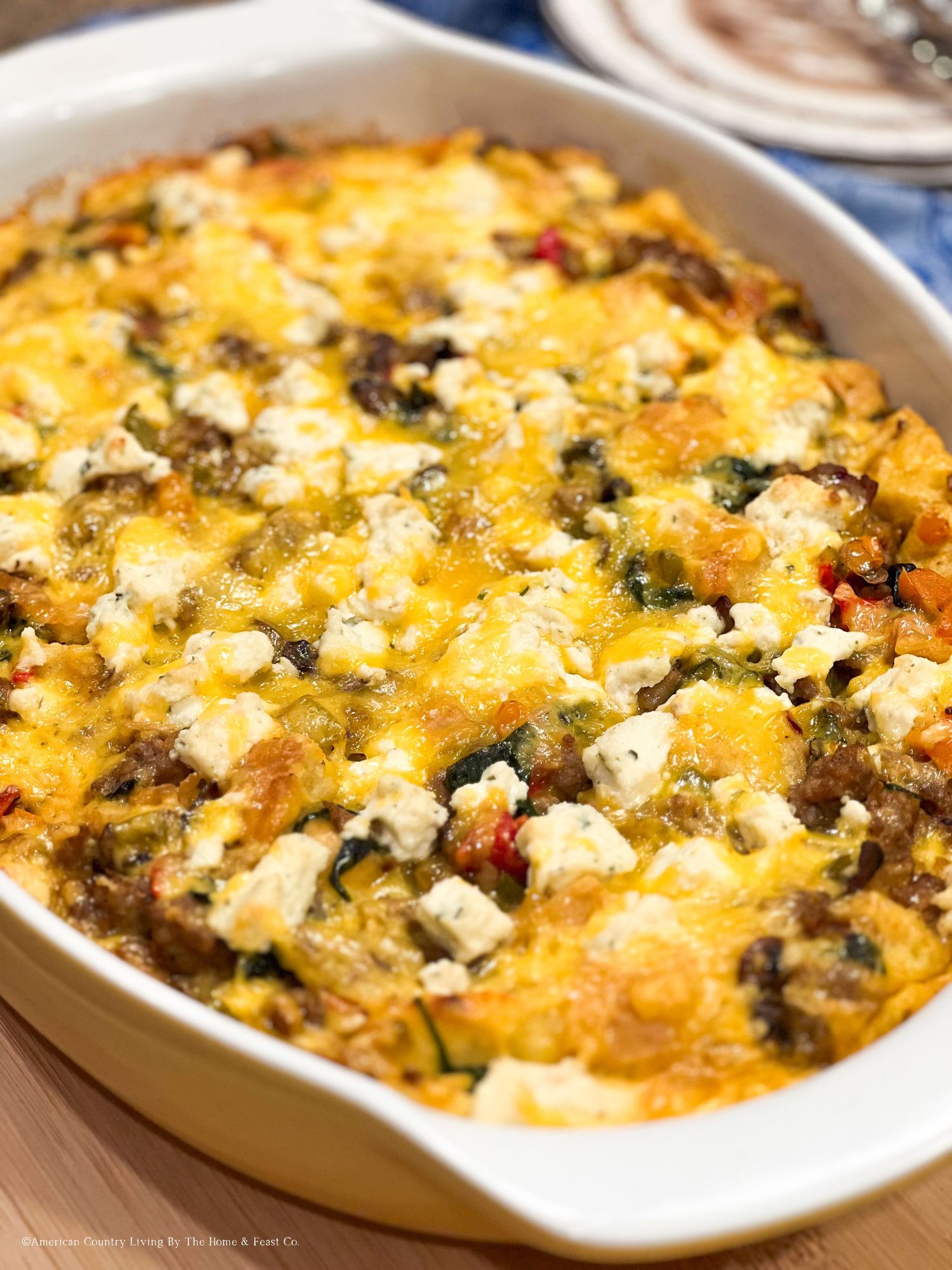 Baked casserole with melted cheese, vegetables and herbs in a white oval dish.