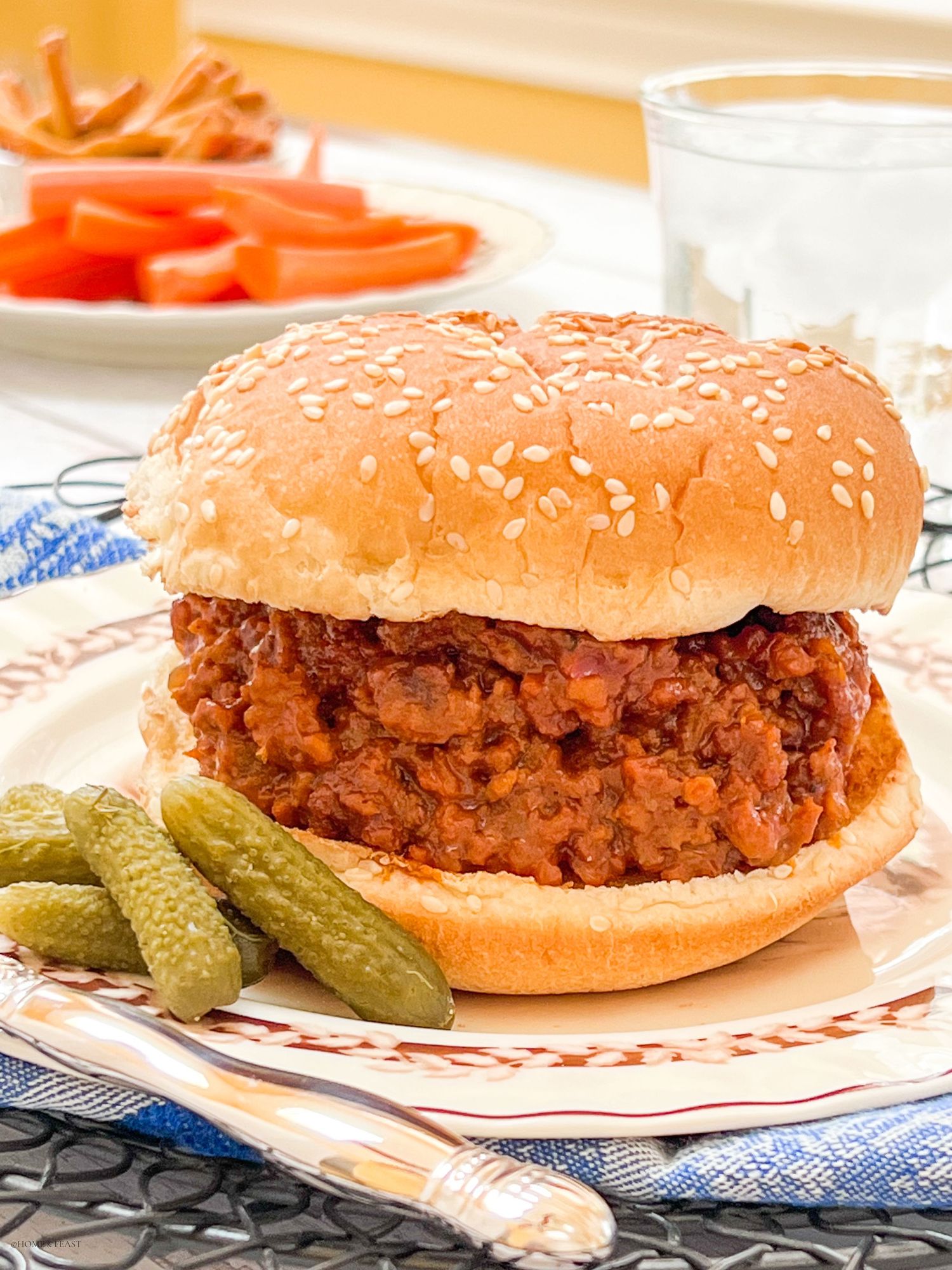Classic sloppy joe sandwich with ground beef filling served on plate with dill pickles.