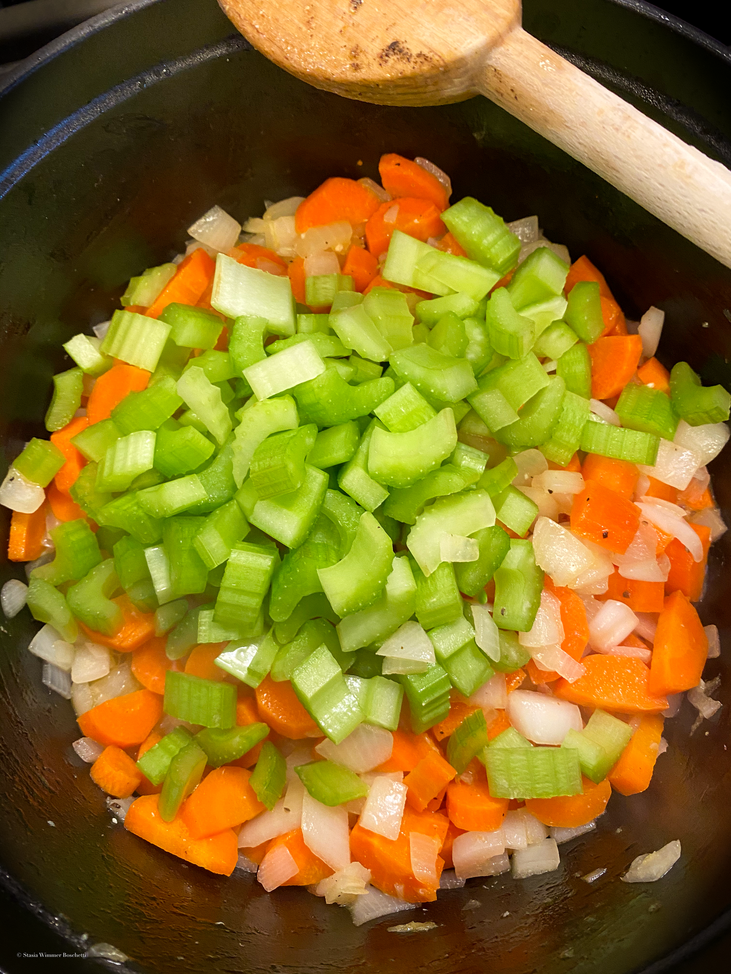 Diced celery, carrots and onions being sautéed in a black pan.
