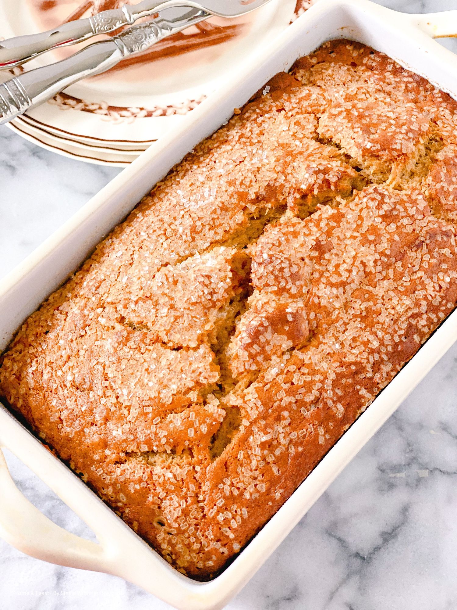 Golden brown quick bread with sugary crust baked in white ceramic loaf pan.
