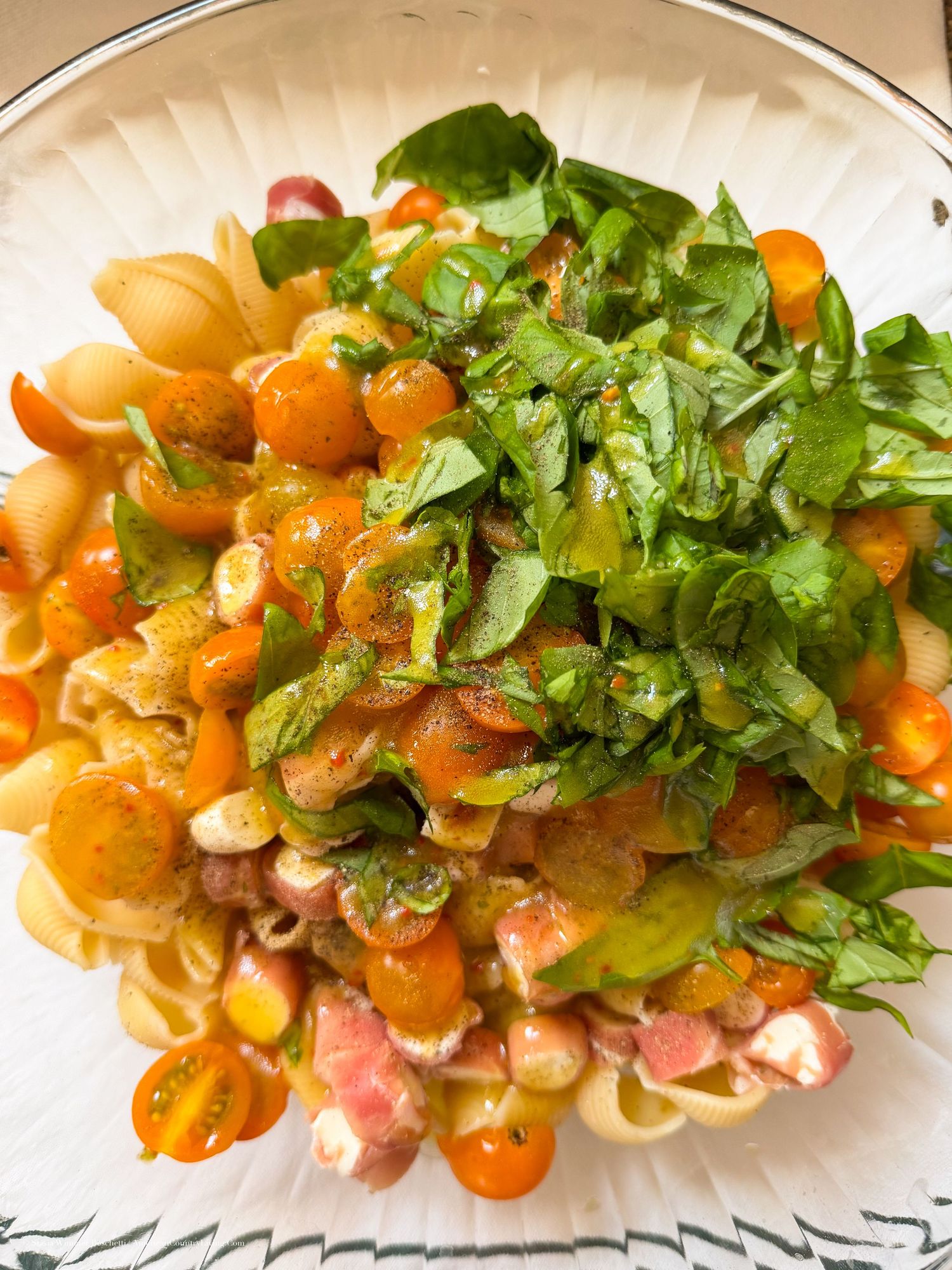 Colorful pasta salad with cherry tomatoes, fresh basil, and mixed greens served on a white plate.