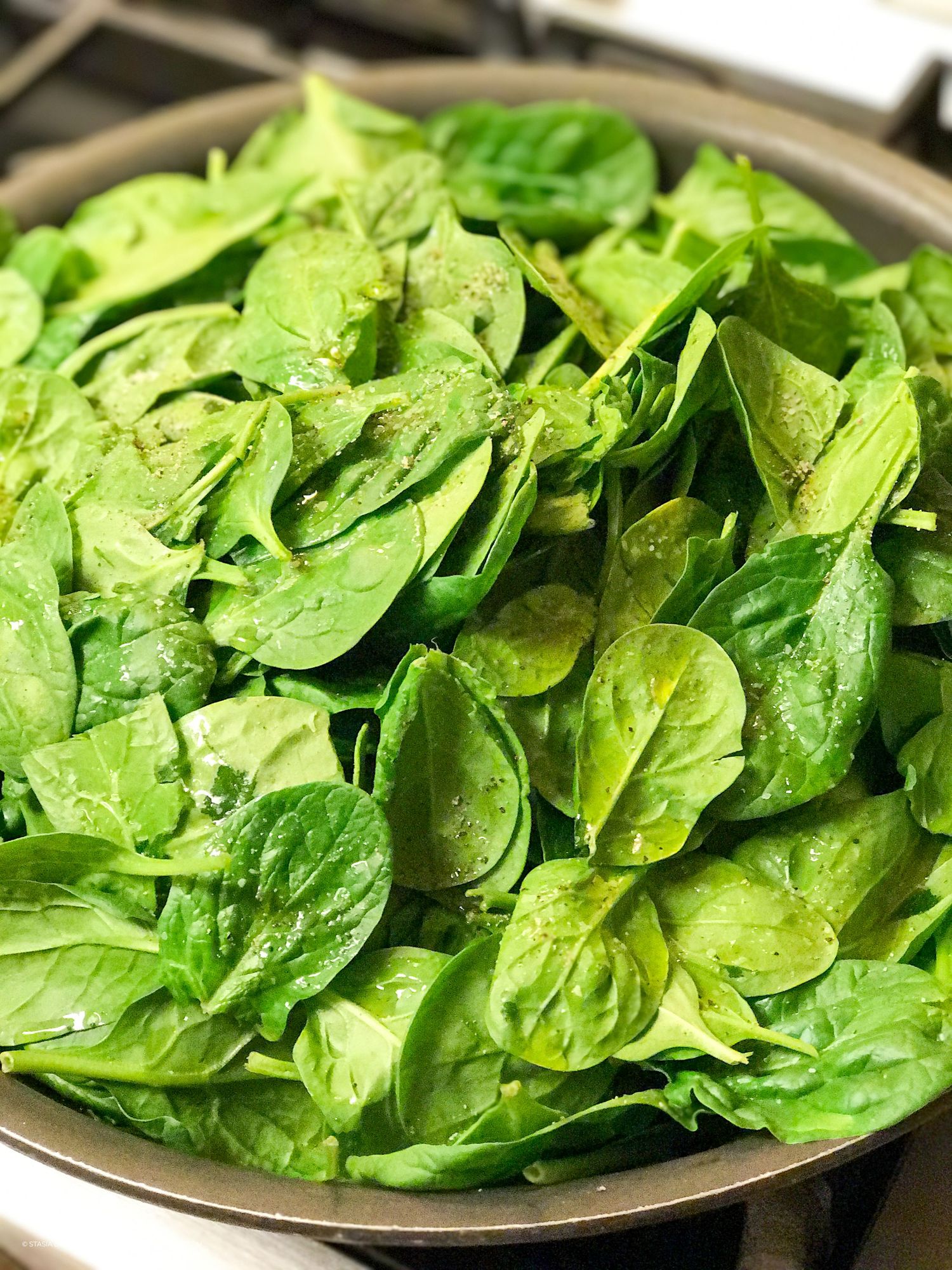 Fresh baby spinach leaves piled high in a pan, ready for cooking.