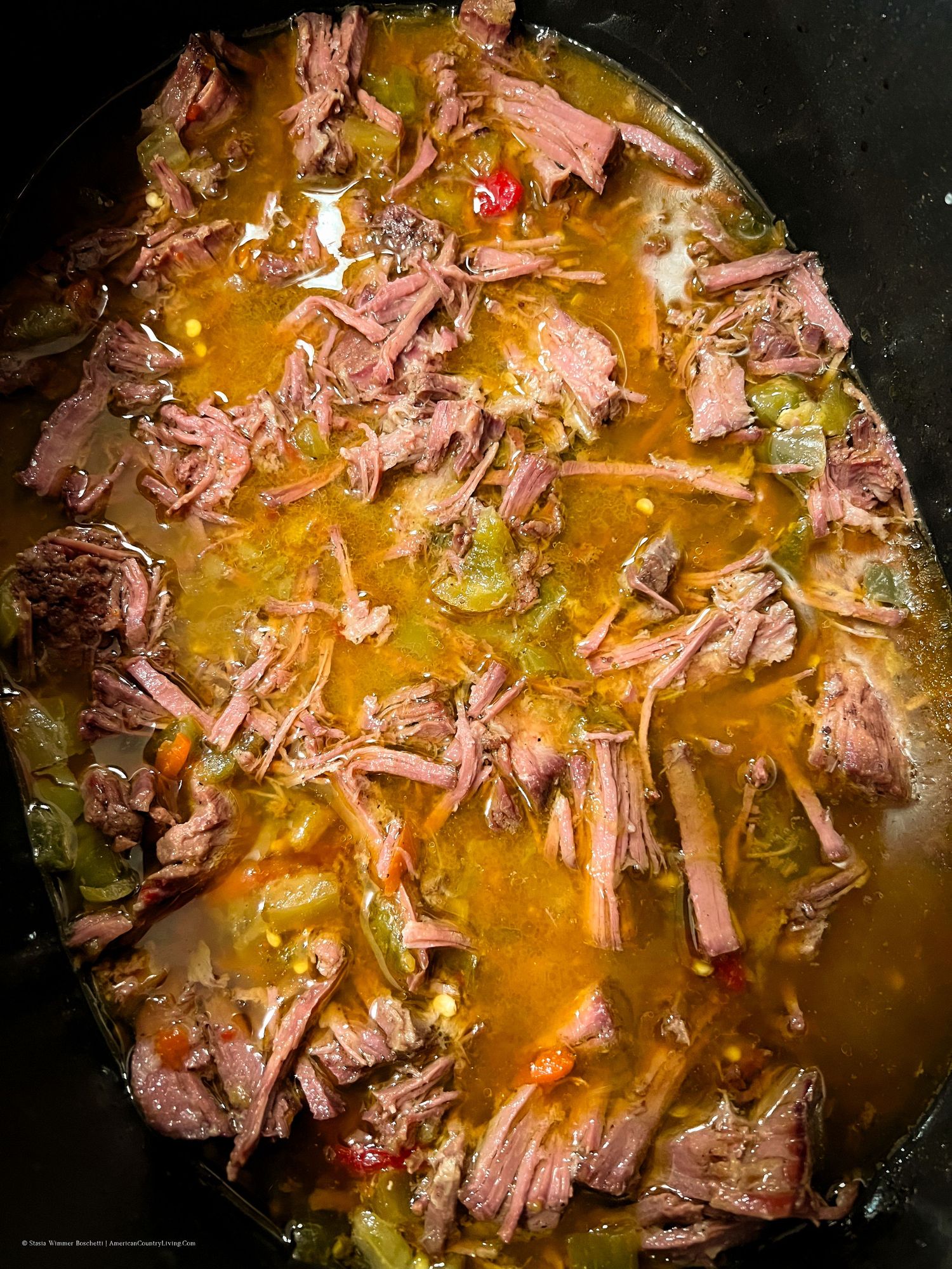 Shredded beef and vegetables simmering in rich sauce in black pan.