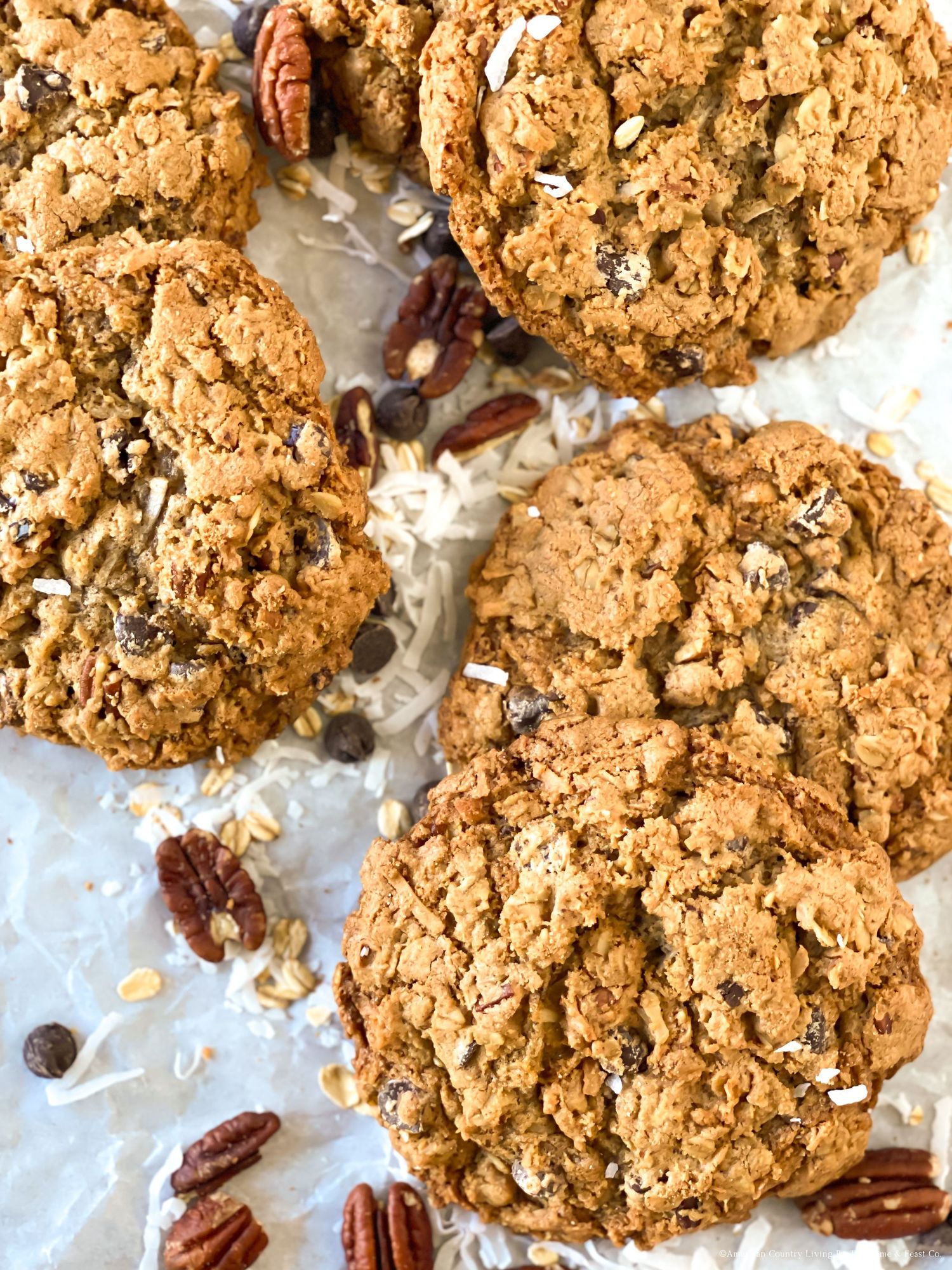 Golden oatmeal cookies with chocolate chips and pecans arranged on parchment paper.