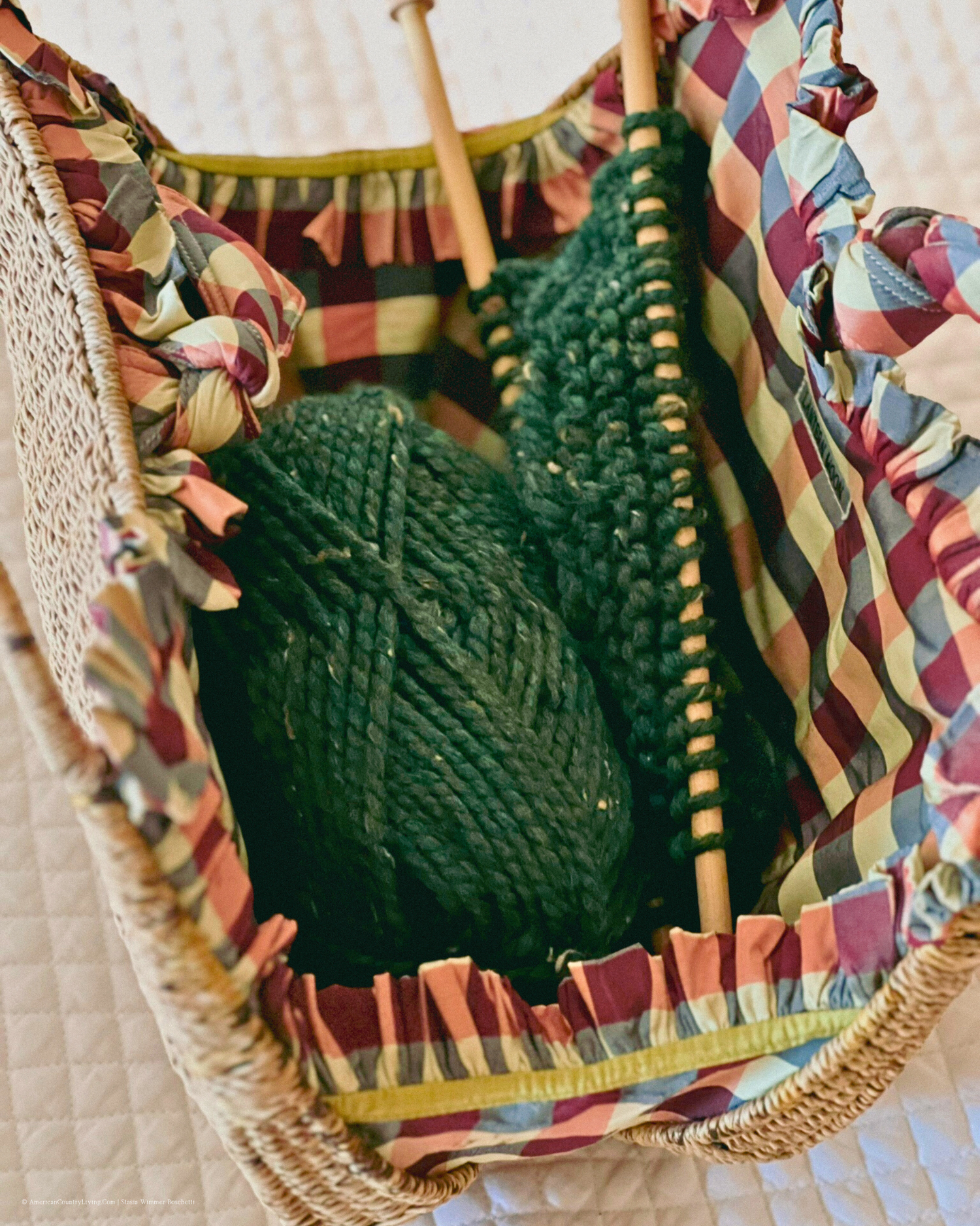 Green yarn and knitting needles in colorful striped fabric basket.