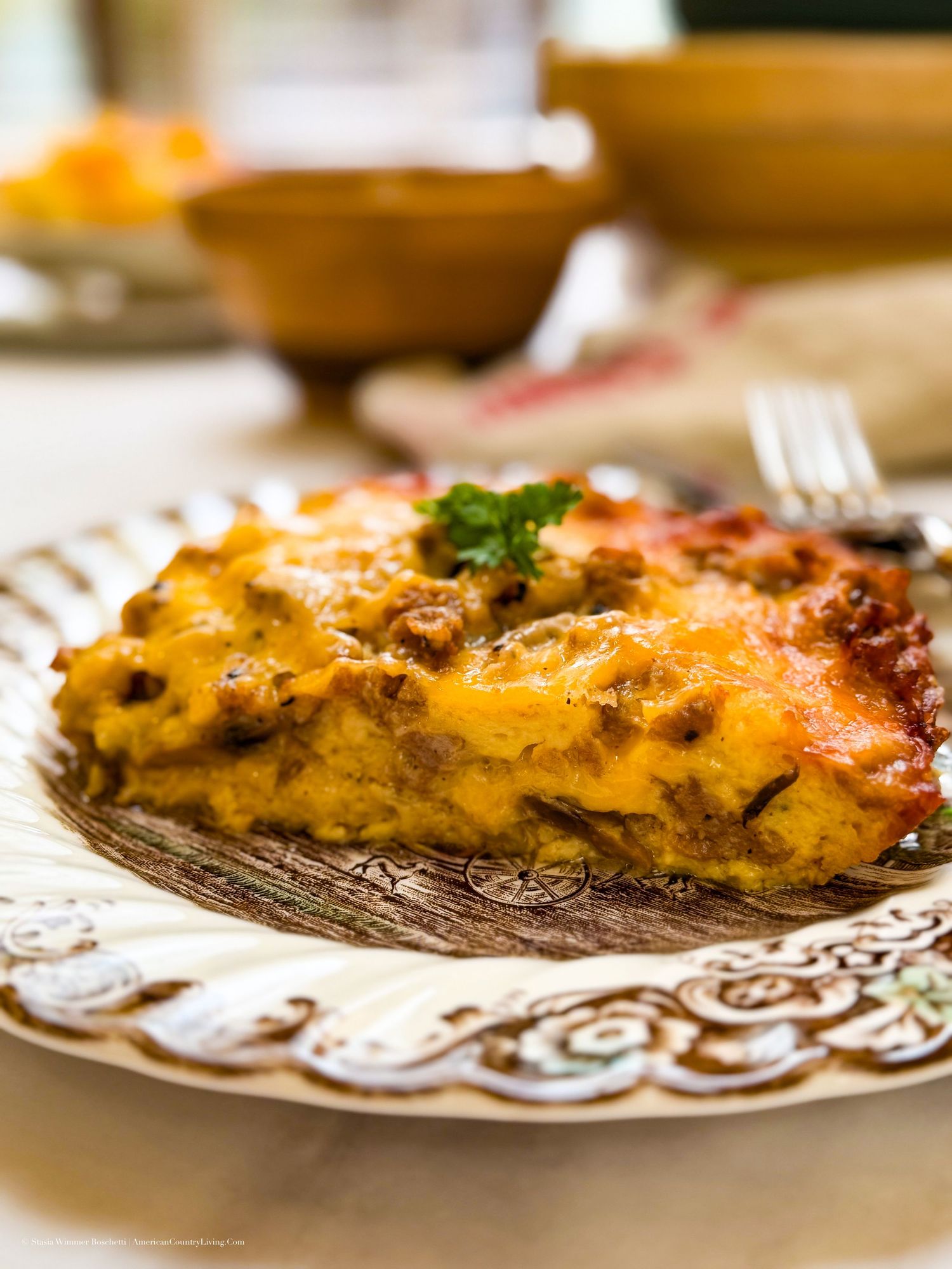 A golden-brown slice of cheesy lasagna on a decorative plate, garnished with fresh parsley, served on a marble surface.