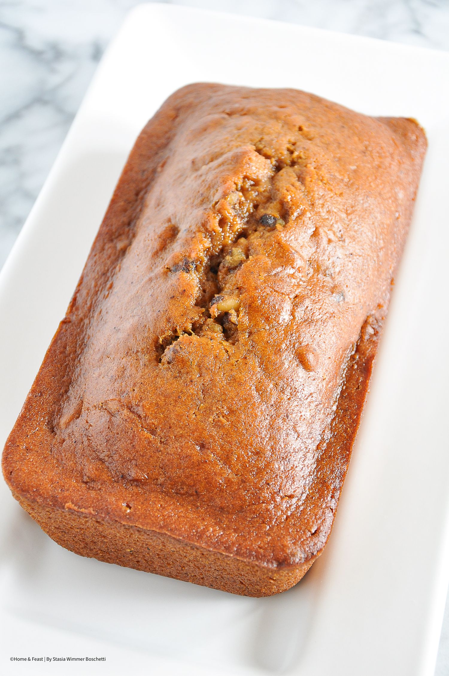 Freshly baked pumpkin loaf cake with golden brown crust on white platter.