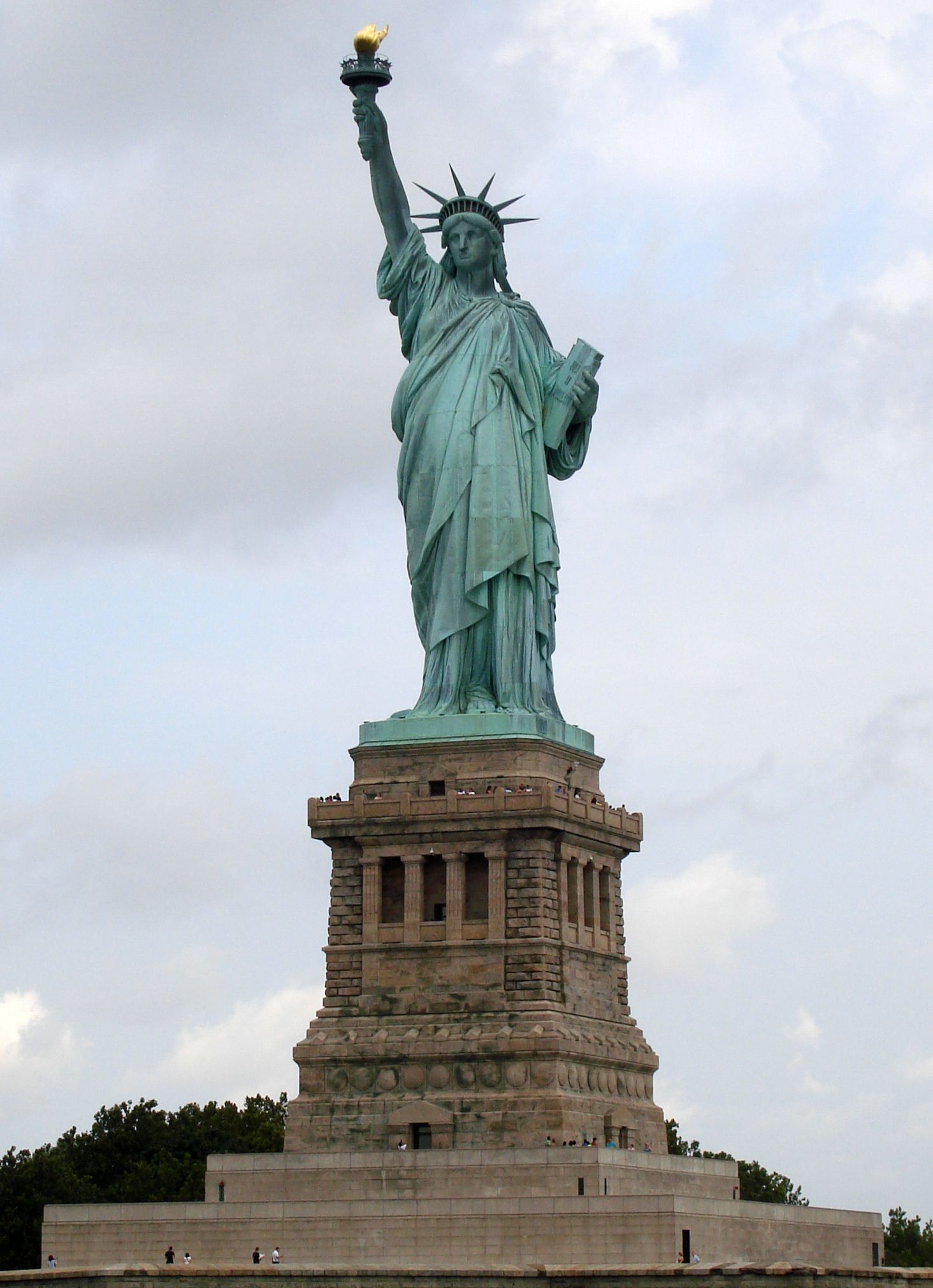 The Statue of Liberty stands majestically against a cloudy sky on Liberty Island in New York Harbor.
