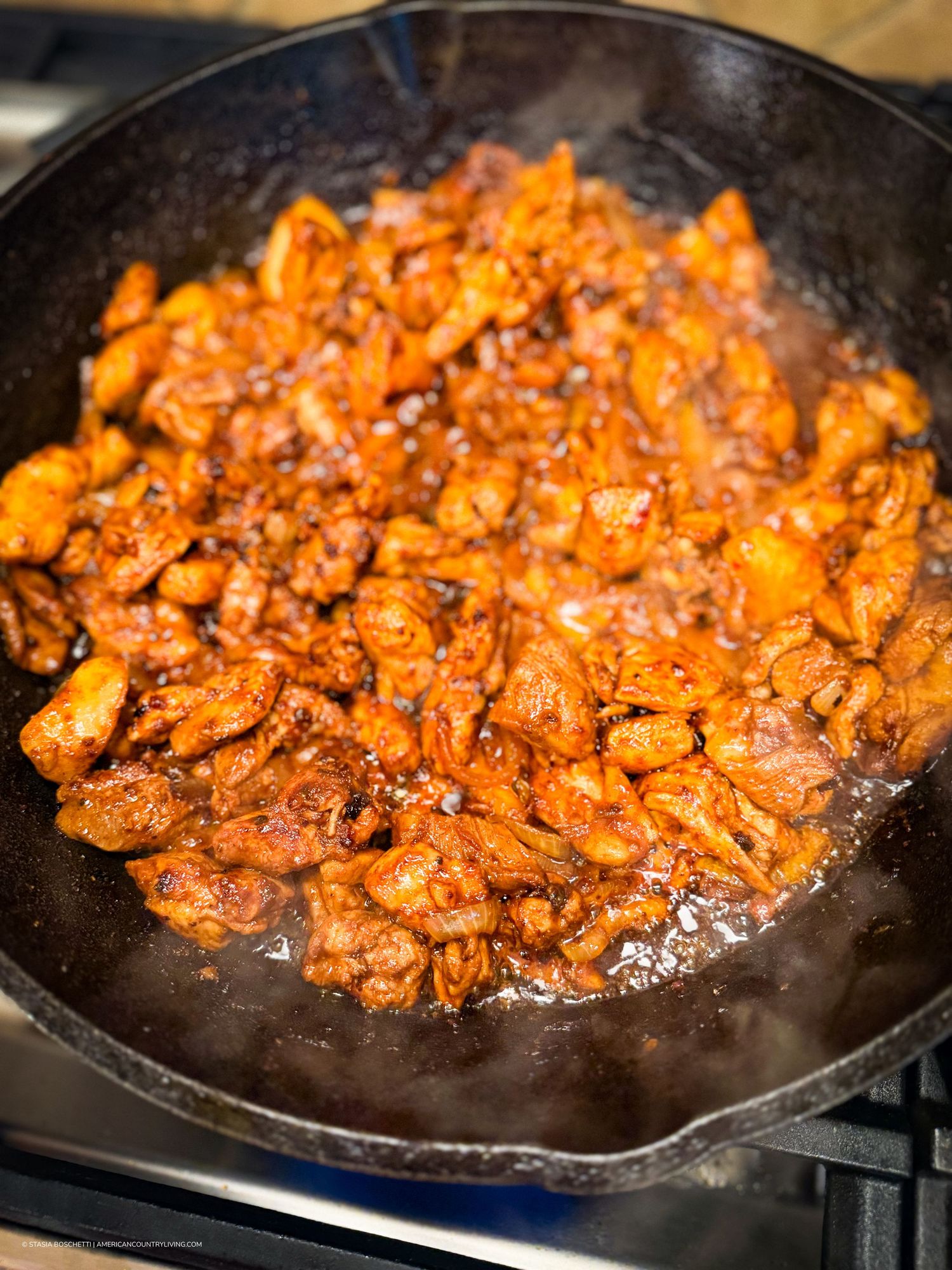 Spicy marinated chicken pieces sizzling in a cast iron skillet with rich red sauce.