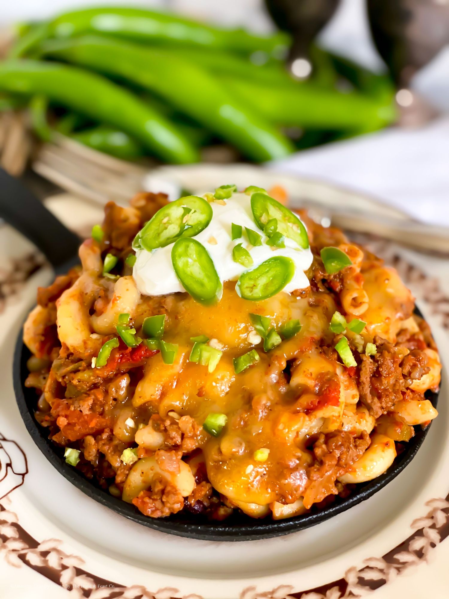 Loaded mac and cheese topped with jalapenos, sour cream, and ground meat on a decorative plate.
