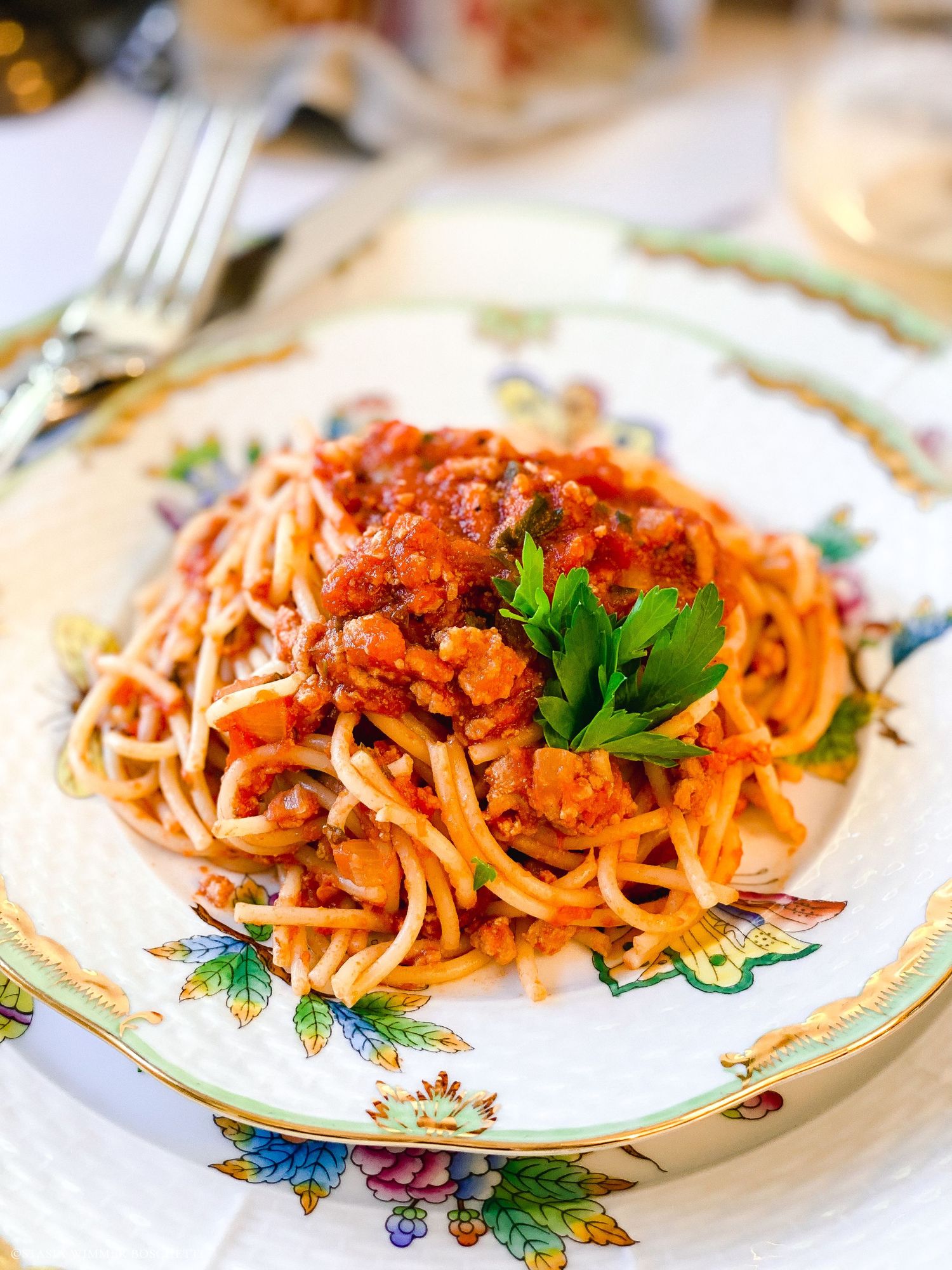Classic spaghetti with meat sauce garnished with parsley on a vintage floral plate.