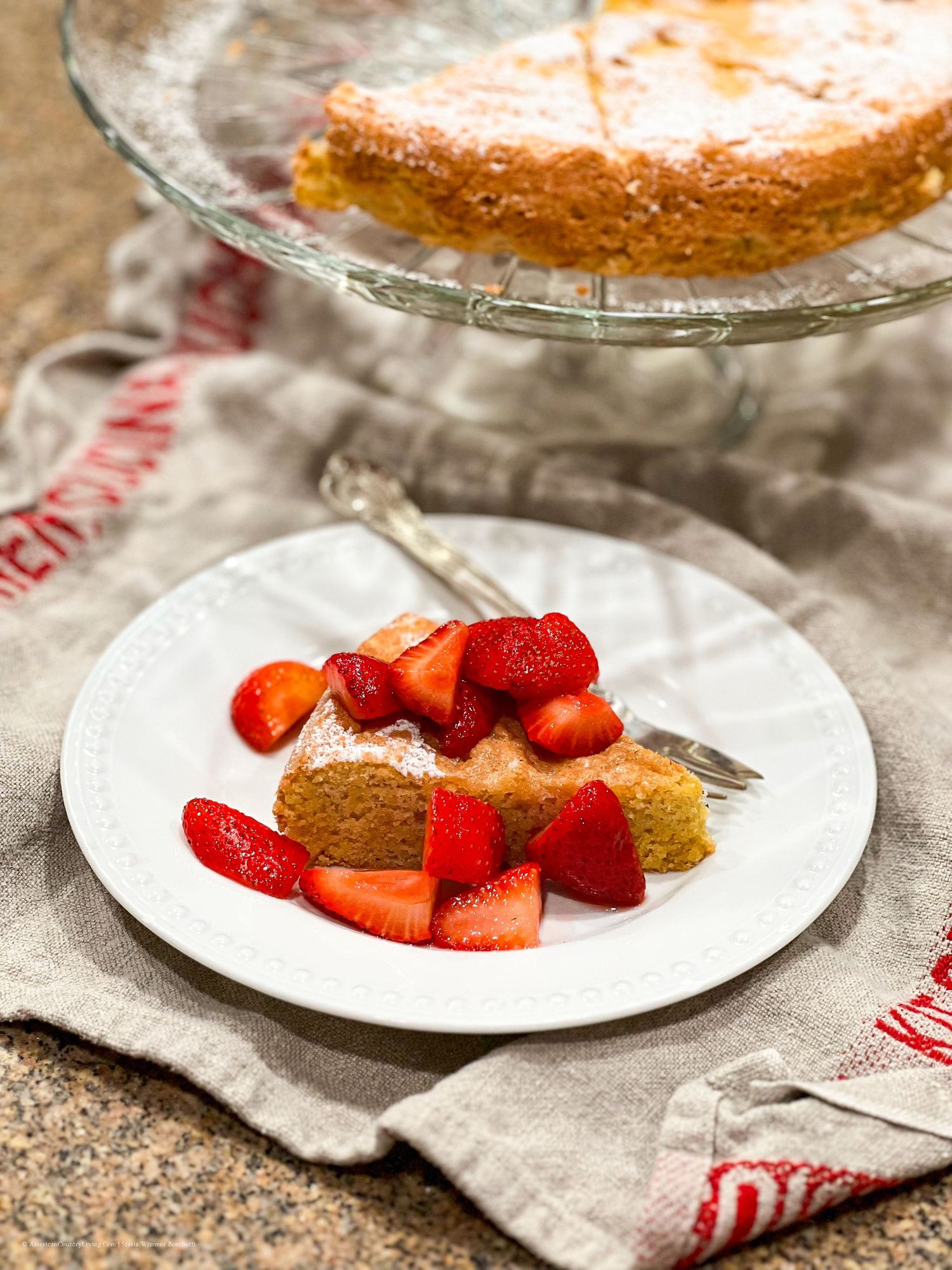 A slice of cake with fresh strawberries served on a white plate with a rustic linen napkin.