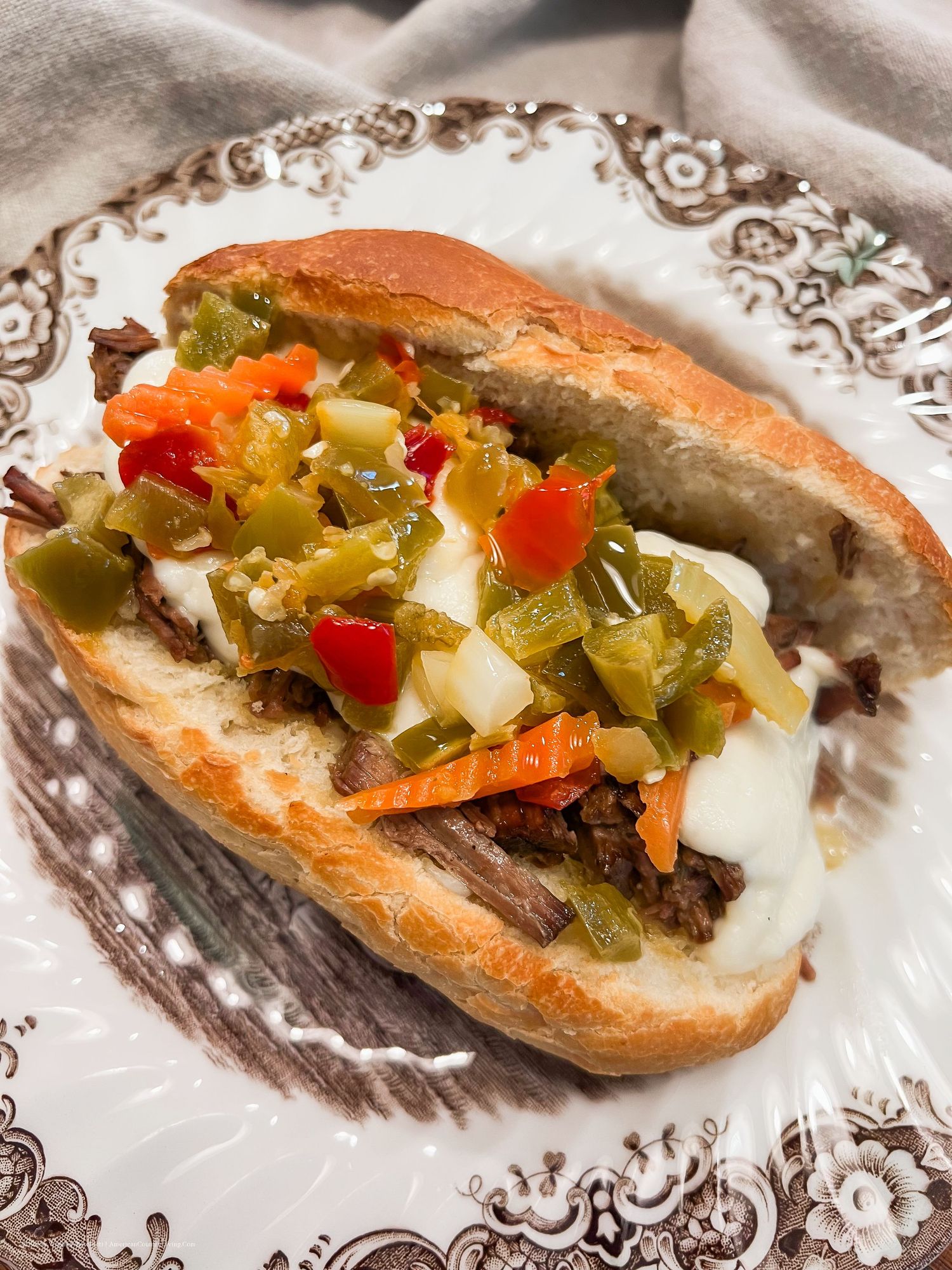 Italian beef sandwich loaded with giardiniera peppers and vegetables on decorative plate.