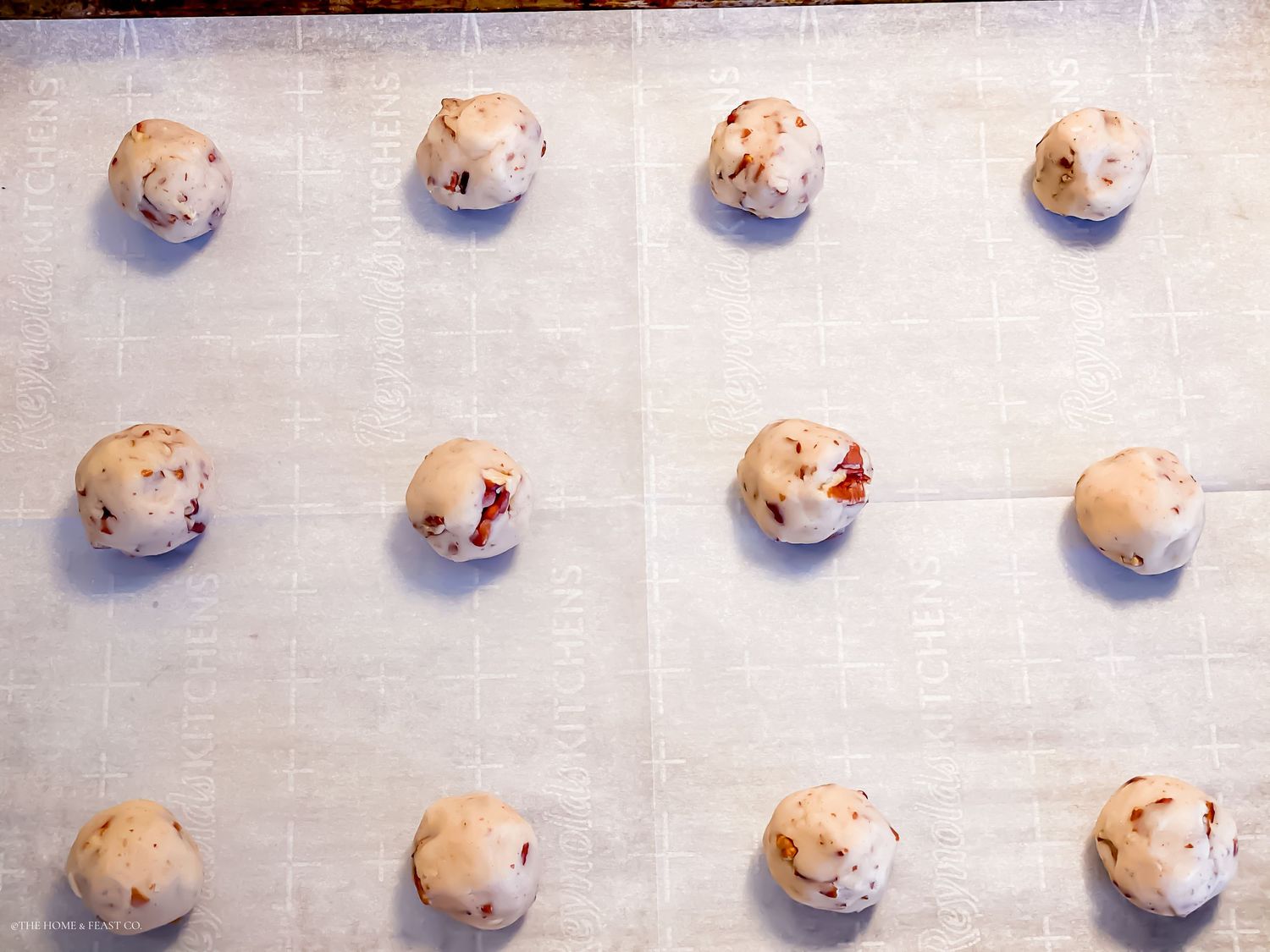 Unbaked cookie dough balls arranged in rows on a parchment-lined baking sheet, ready to bake.