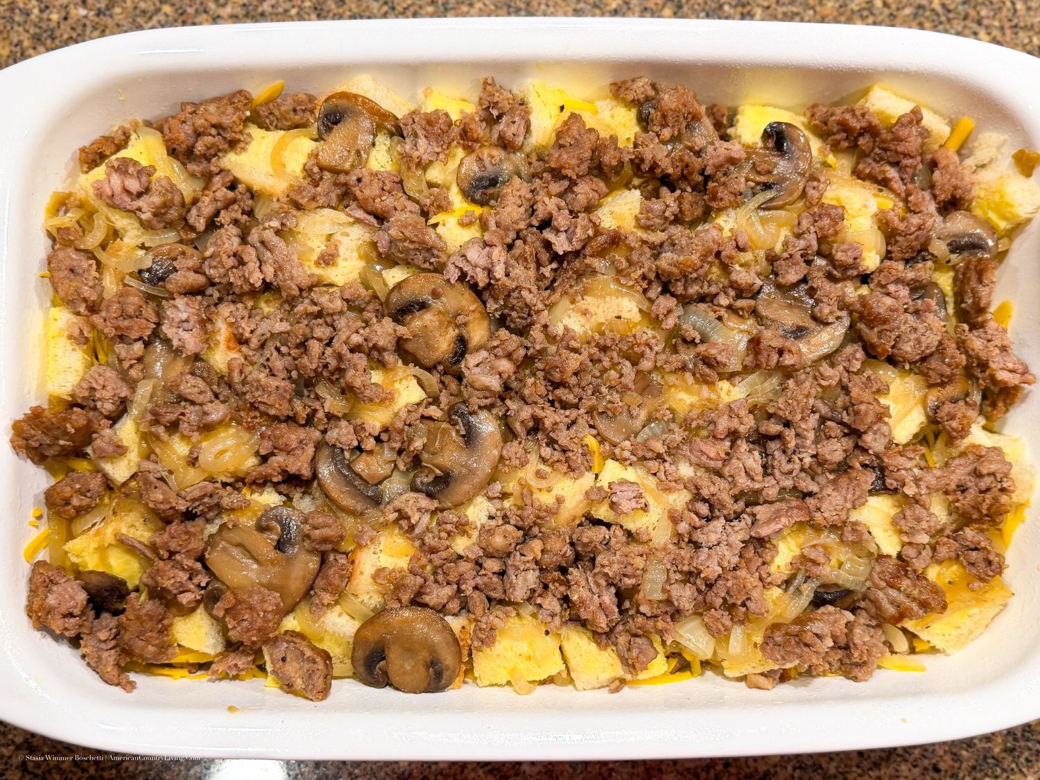 Baked casserole dish with ground beef, mushrooms, and melted cheese over a golden egg base.