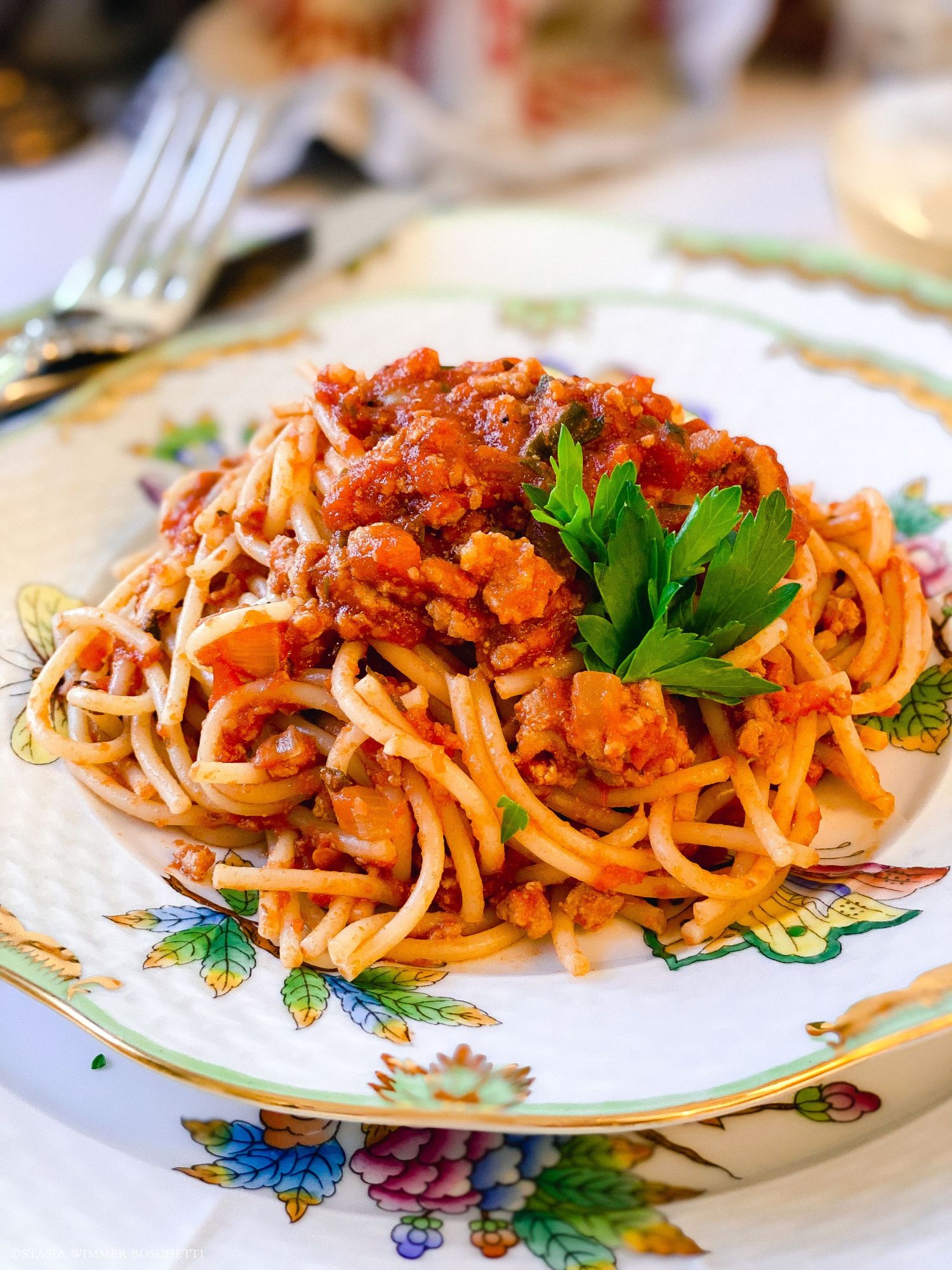 Spaghetti with rich tomato meat sauce and fresh parsley garnish served on a floral patterned plate.