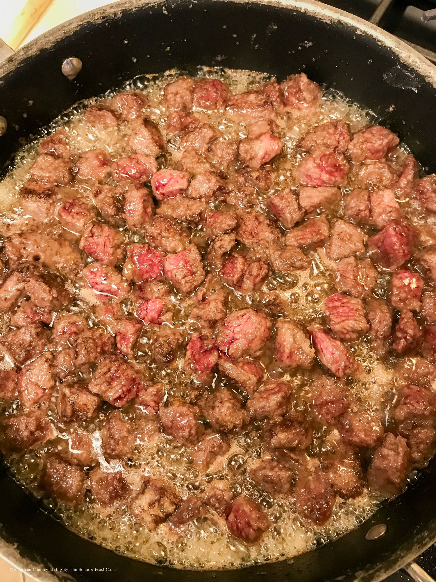 Beef chunks browning in a cast iron skillet with seasonings and butter.
