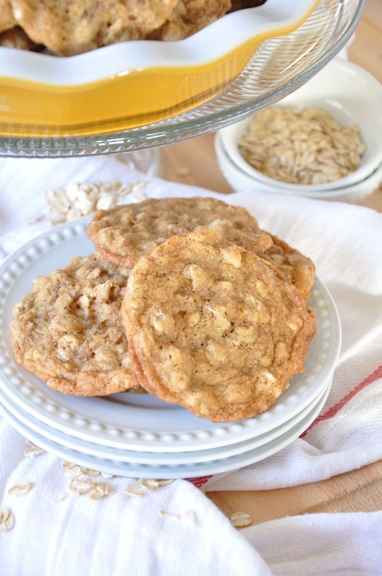 Homemade oatmeal cookies stacked on plates with raw oats in background.