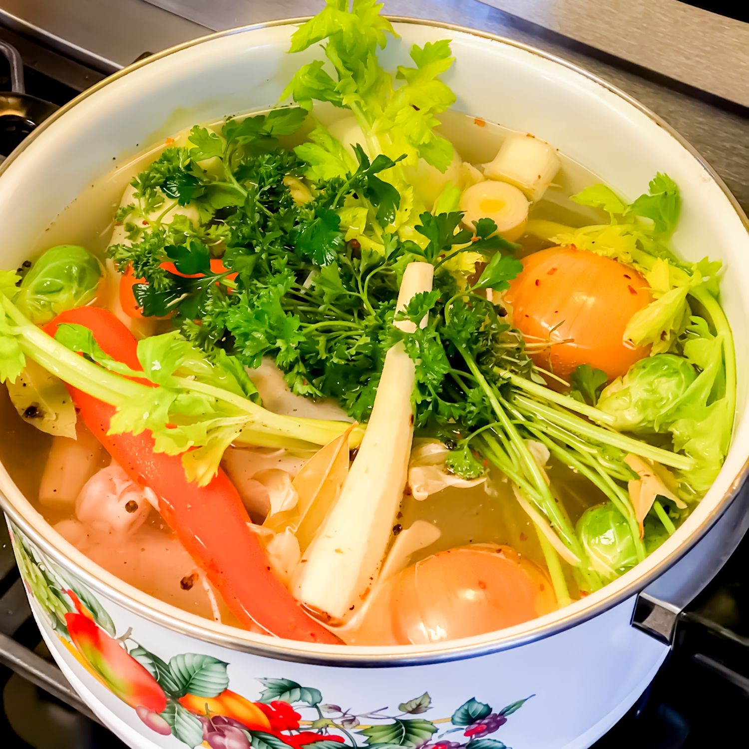 Colorful pot of vegetables and herbs simmering in broth with fresh celery and tomatoes.