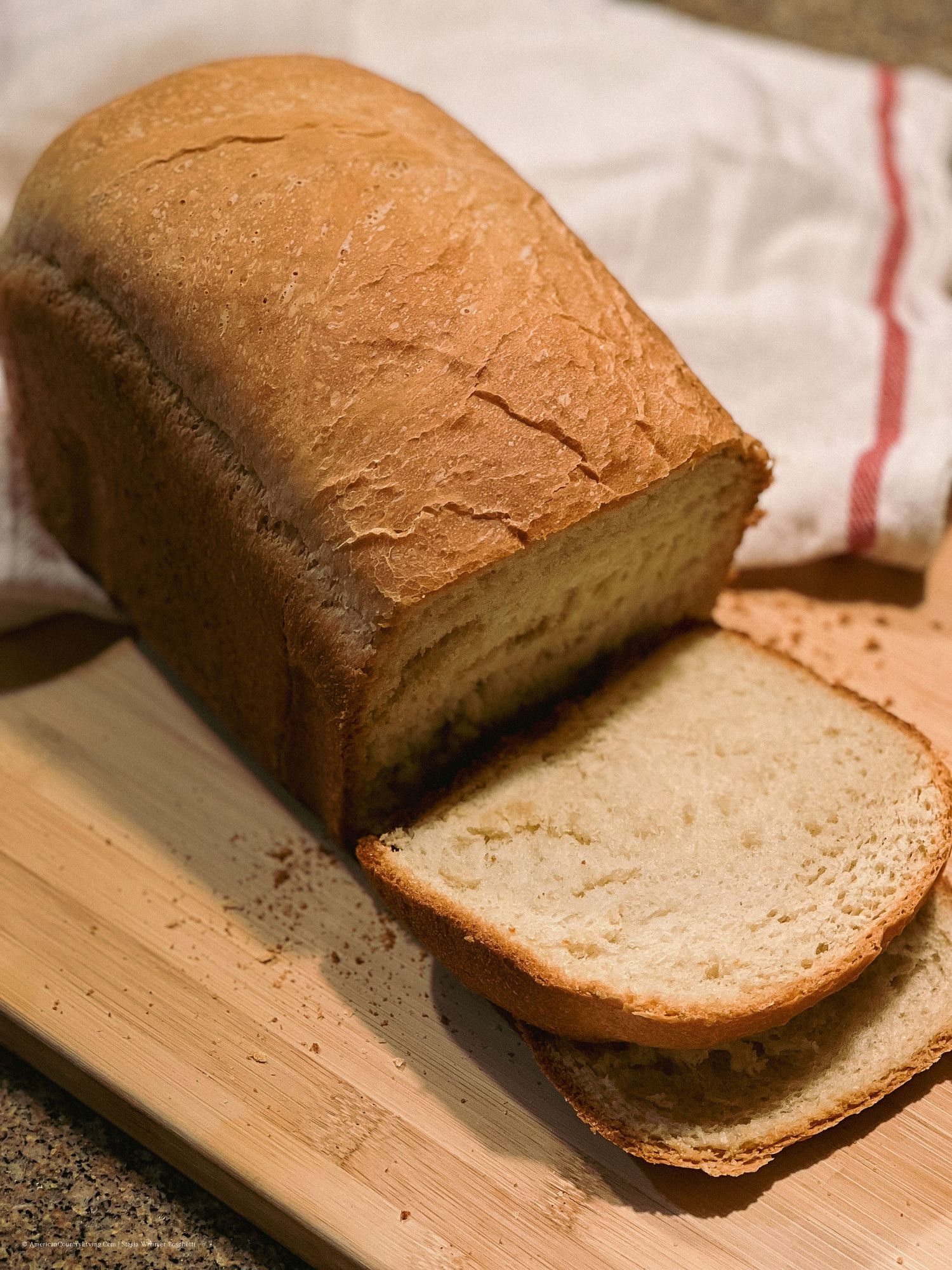 Freshly baked homemade bread loaf sliced on wooden cutting board.