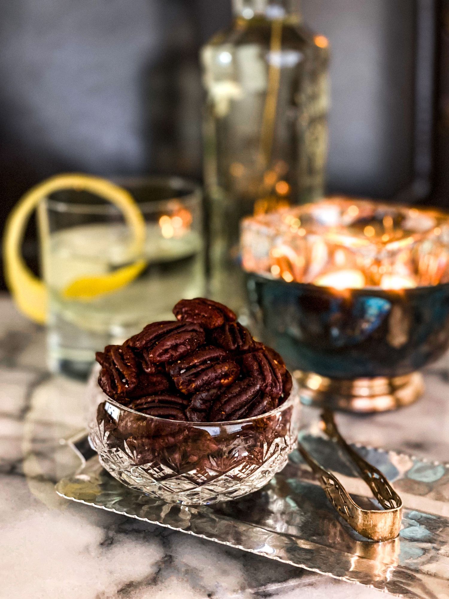Glazed pecans in a cut crystal dish with atmospheric lighting and marble background.