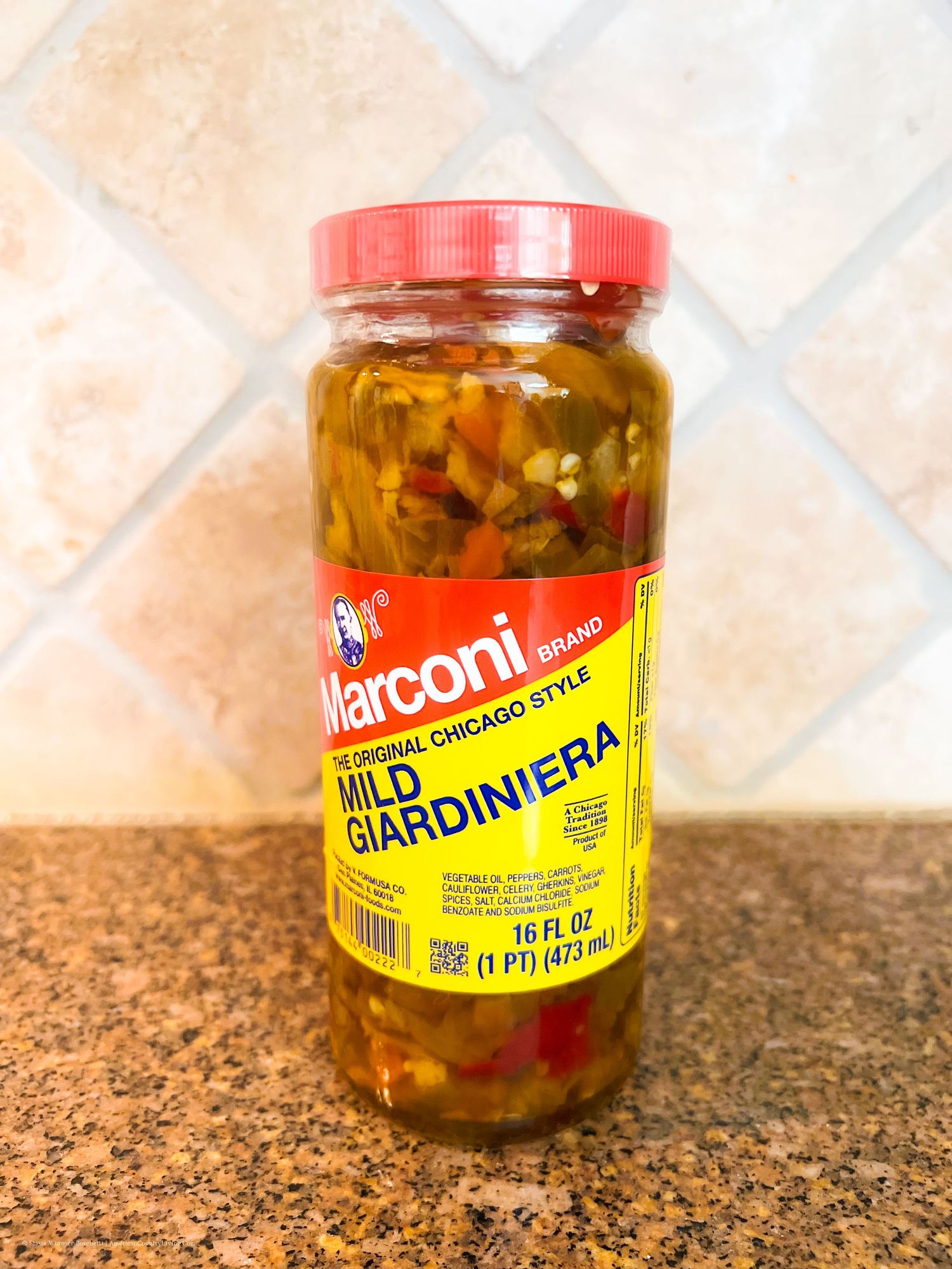 Glass jars of Marconi brand giardiniera peppers on granite countertop.