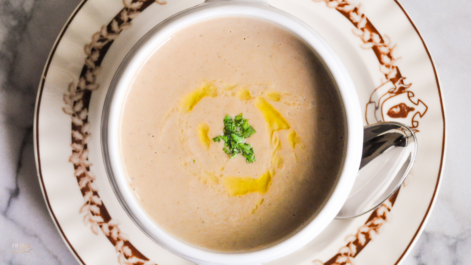 Creamy soup with yellow oil drizzle and green herbs in elegant white bowl.