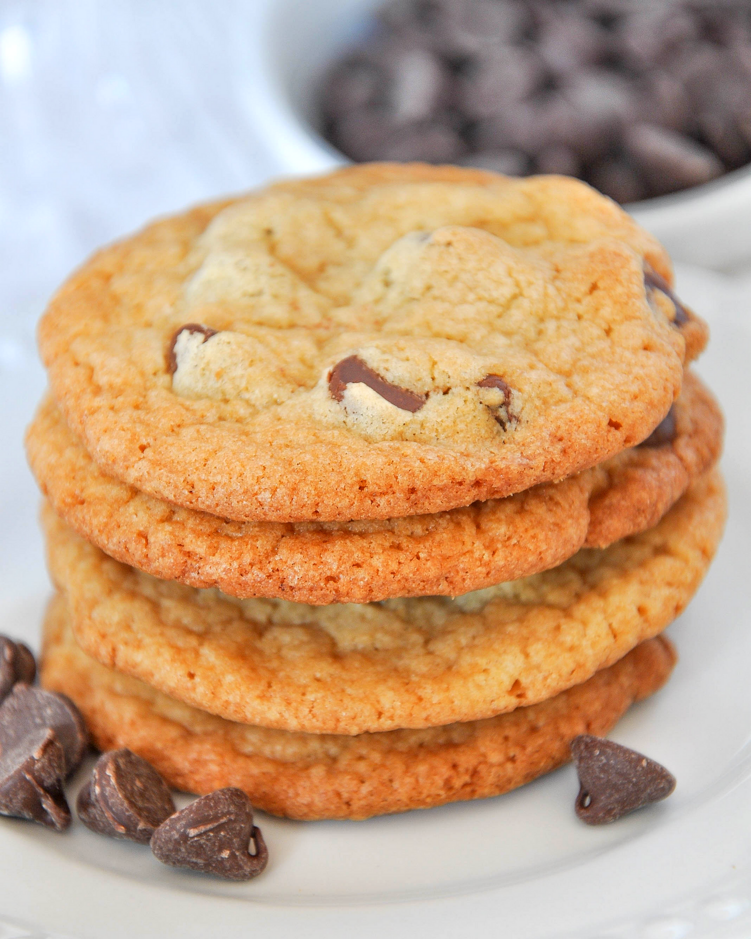 Stack of homemade chocolate chip cookies with scattered chocolate chips on a white plate.