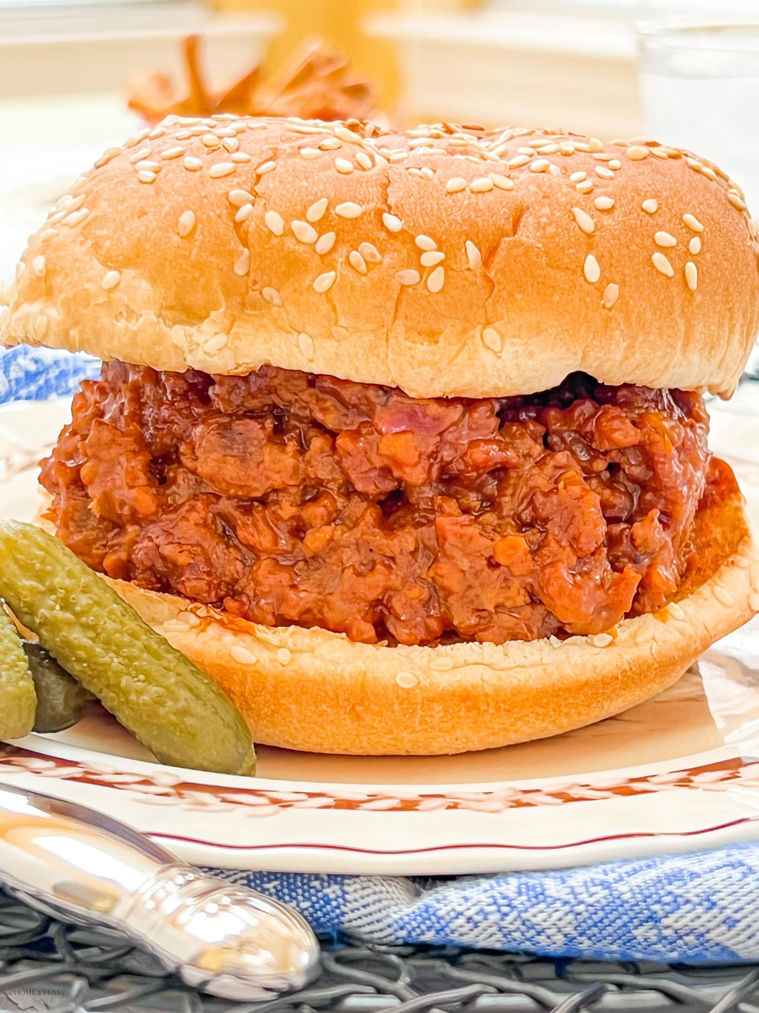 Close up of meaty sloppy joe sandwich with sesame seed bun and pickle garnish.