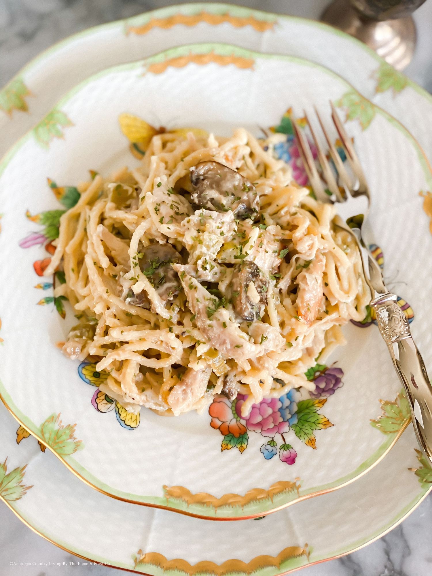 Creamy pasta dish served on decorative floral plates with herbs and sauce.
