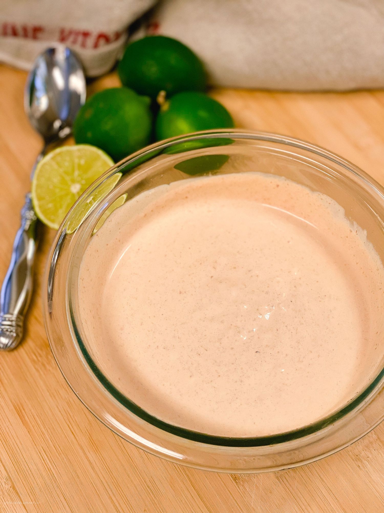 Homemade creamy dressing in a clear glass bowl with fresh ingredients.
