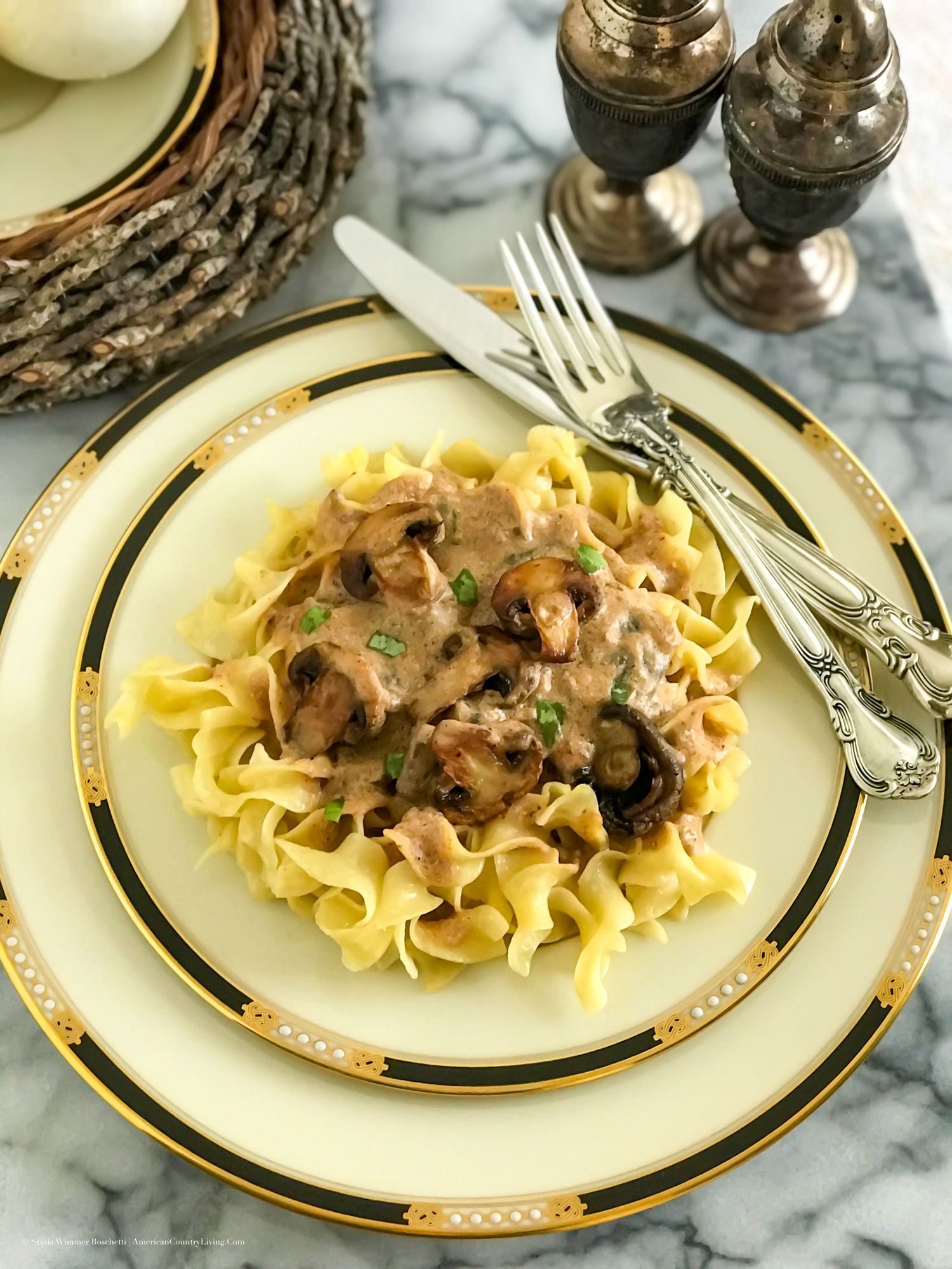 Beef stroganoff with mushrooms over egg noodles on a gold-rimmed plate with silverware.