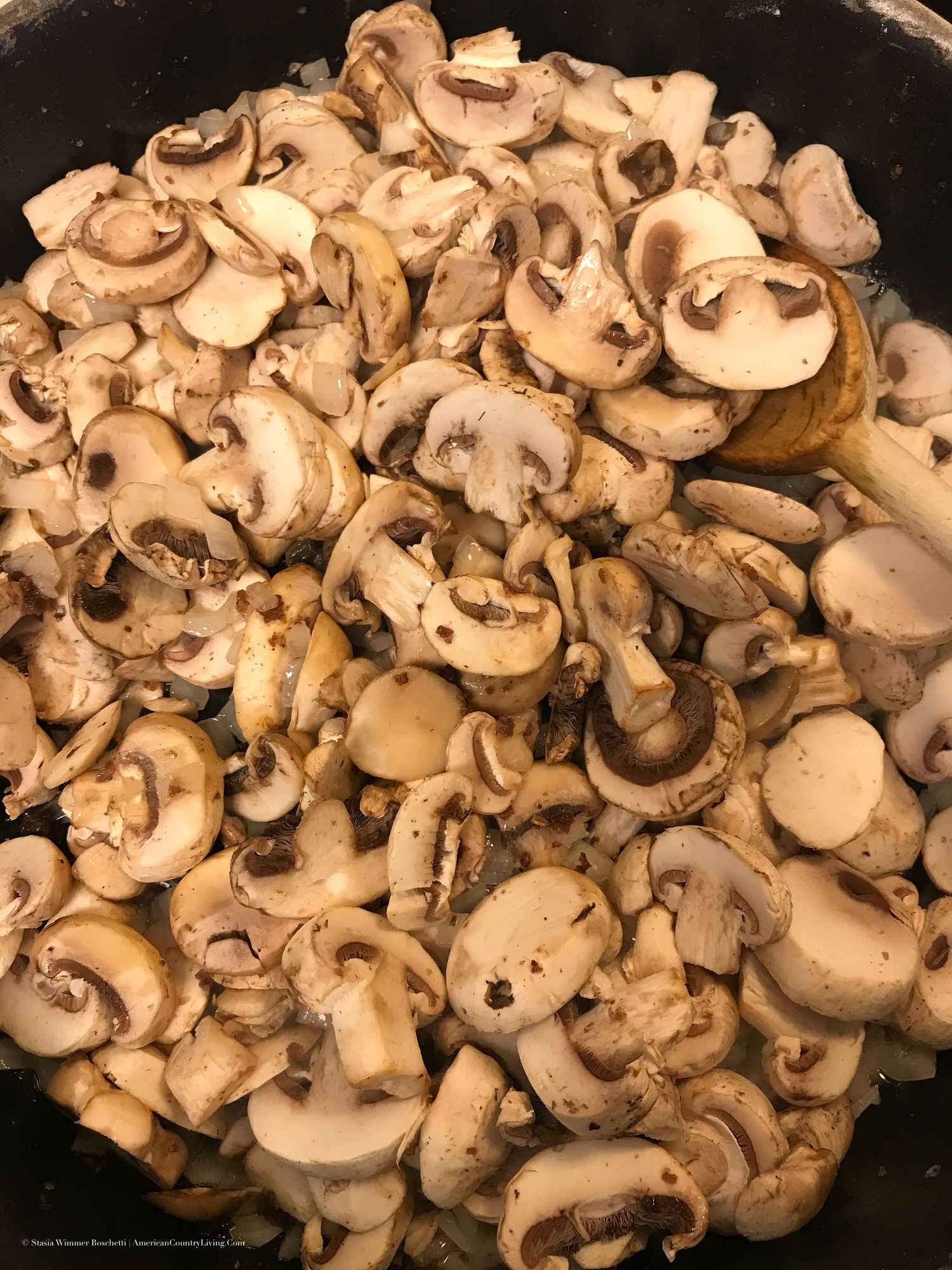 Sliced fresh mushrooms filling a cast iron skillet before cooking.
