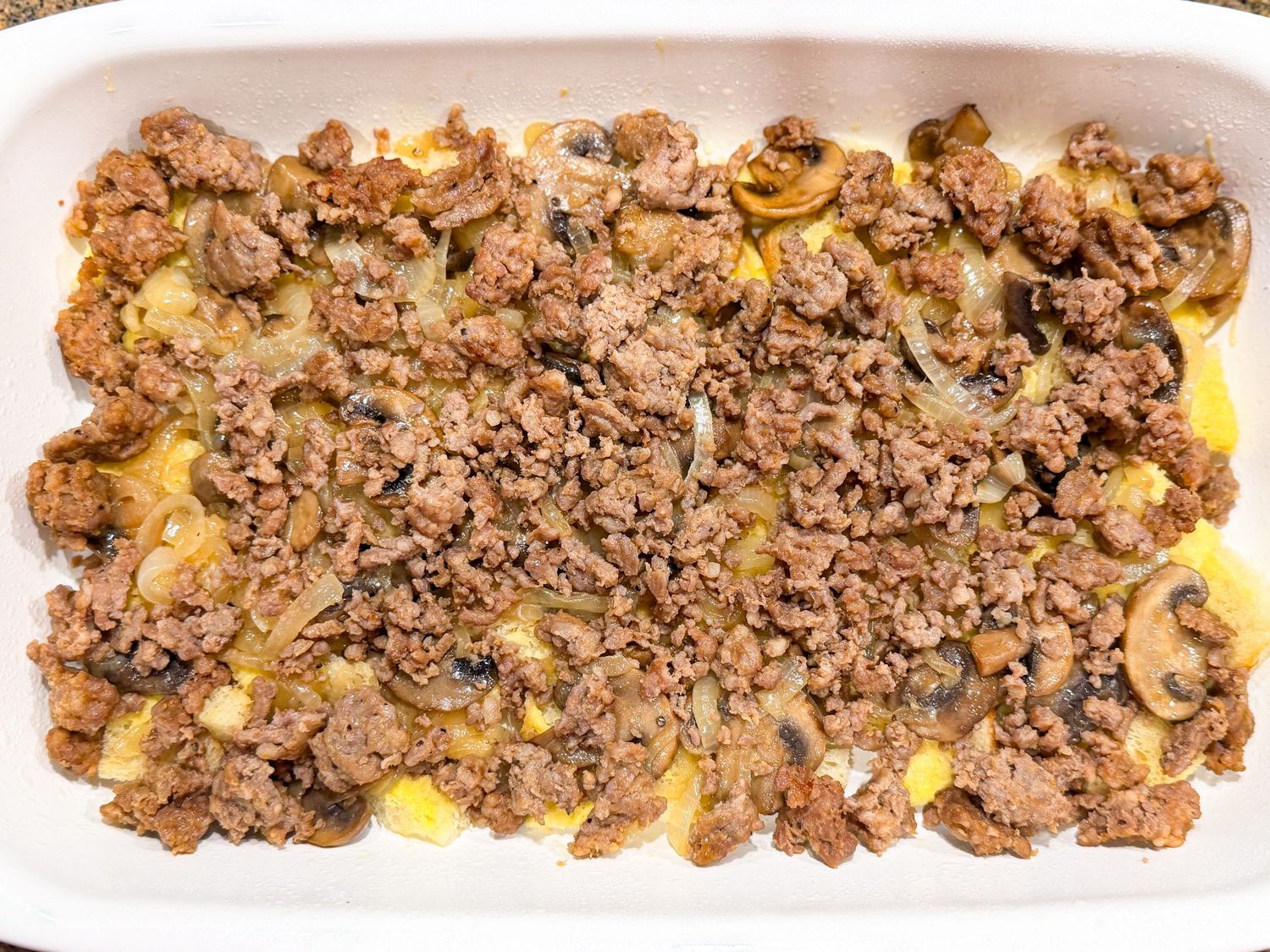 Baked casserole dish with seasoned ground beef, sautéed mushrooms, and onions over a cheesy egg layer.