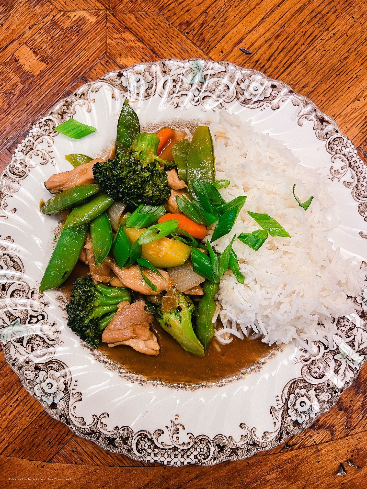 Plated Asian stir fry with steamed white rice served on an ornate white dish with brown sauce.