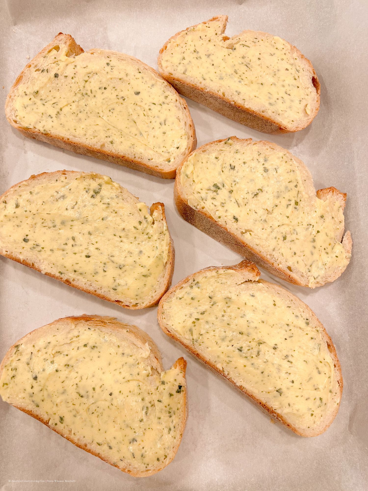 Diagonal slices of herb-seasoned bread laid out in neat rows on a light gray surface.