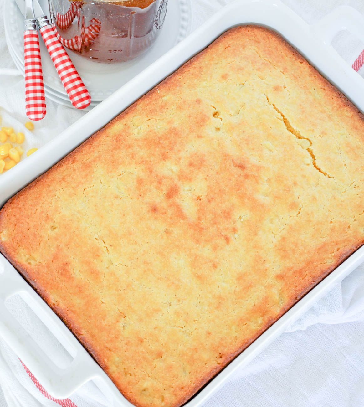 Homemade cornbread with golden brown crust baked in a white baking dish.