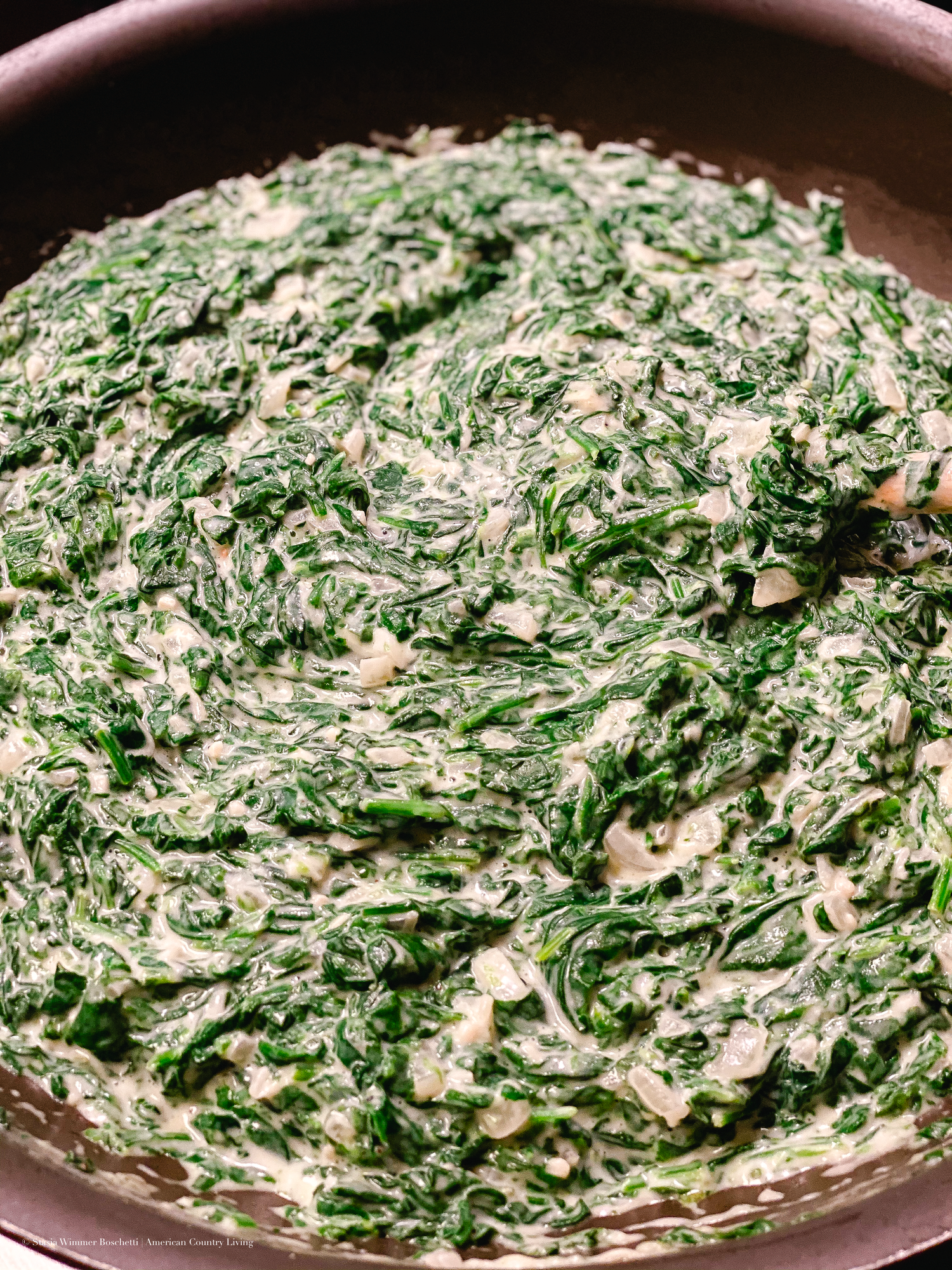Creamy spinach dip mixed with melted cheese shown cooking in a large pan.